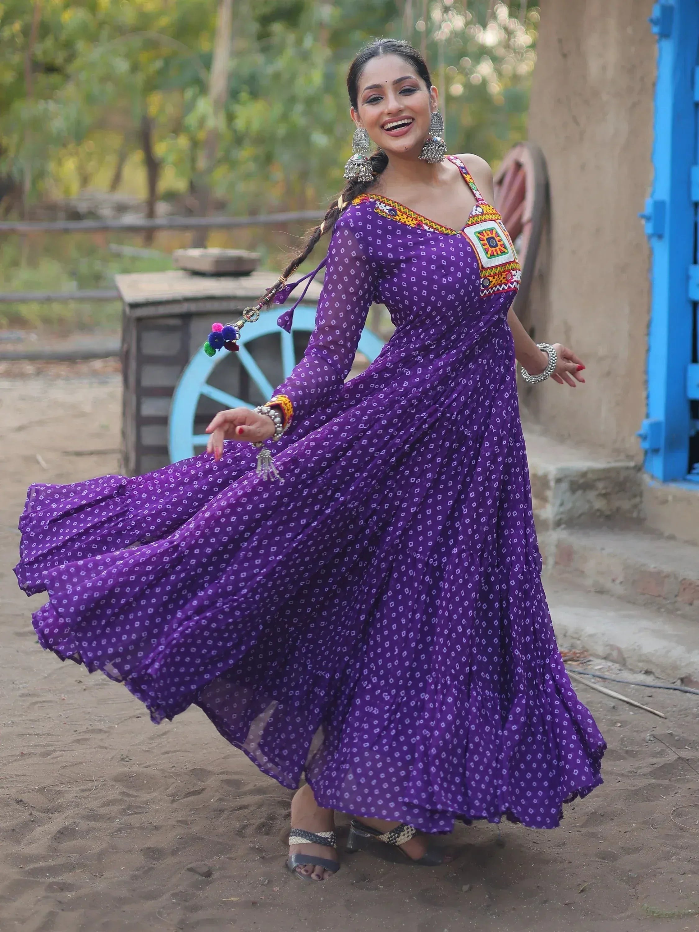 Woman in purple printed ethnic gown with mirror work, dancing outdoors near blue door