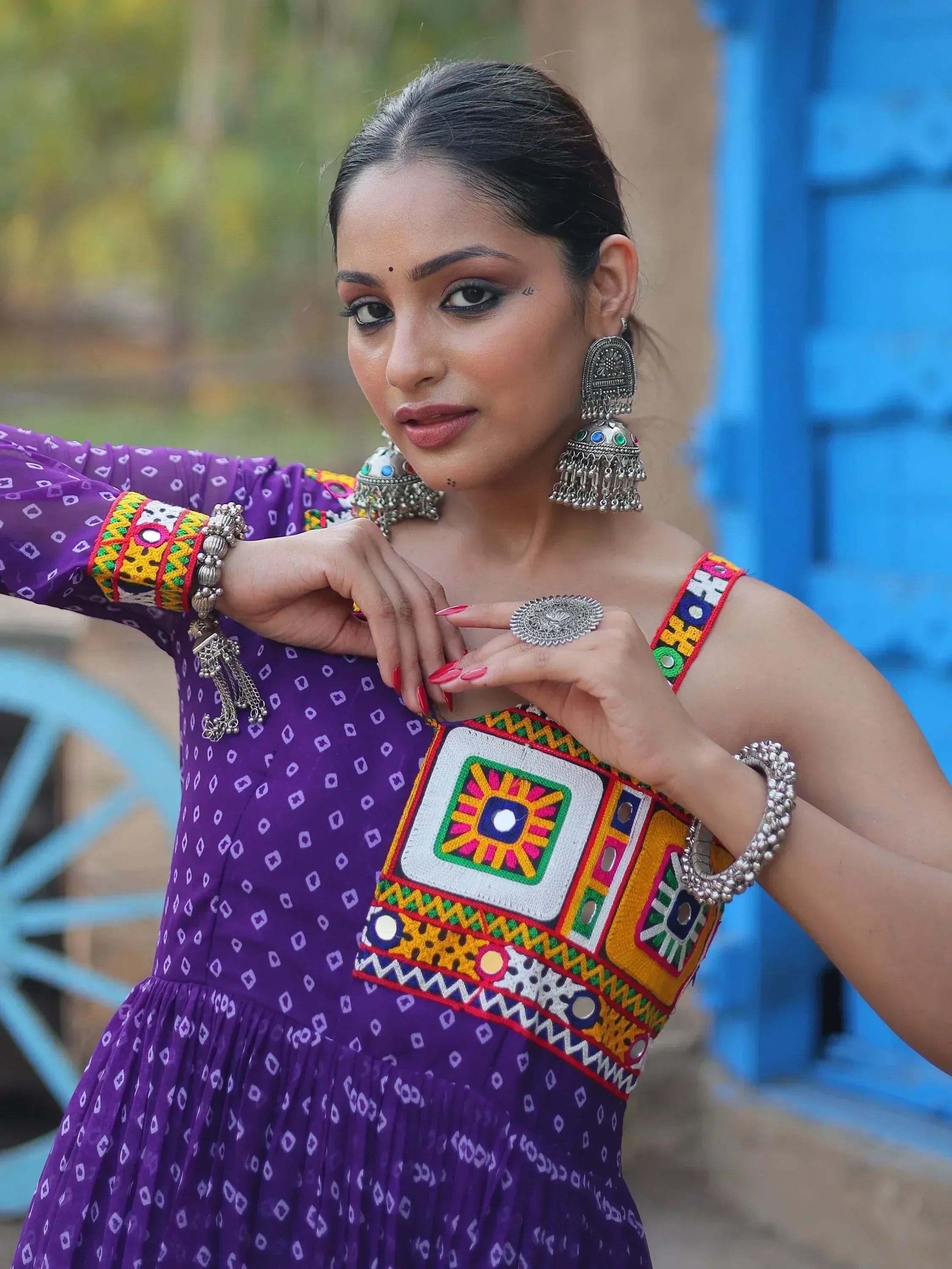 Purple ethnic gown with mirror work, colorful embroidery, and traditional jewelry for Indian wear