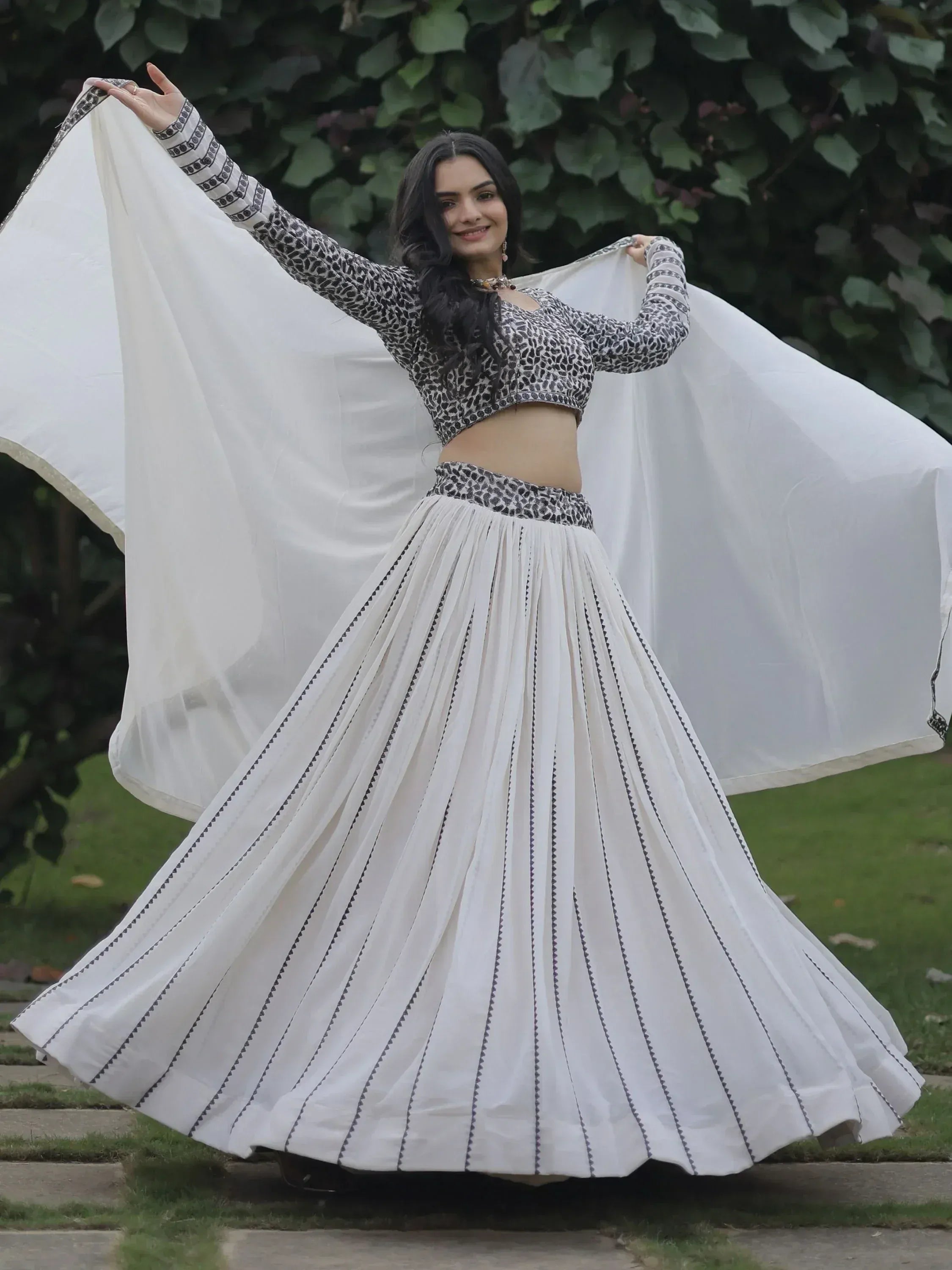 Woman in white pleated lehenga choli with black print, twirling outdoors