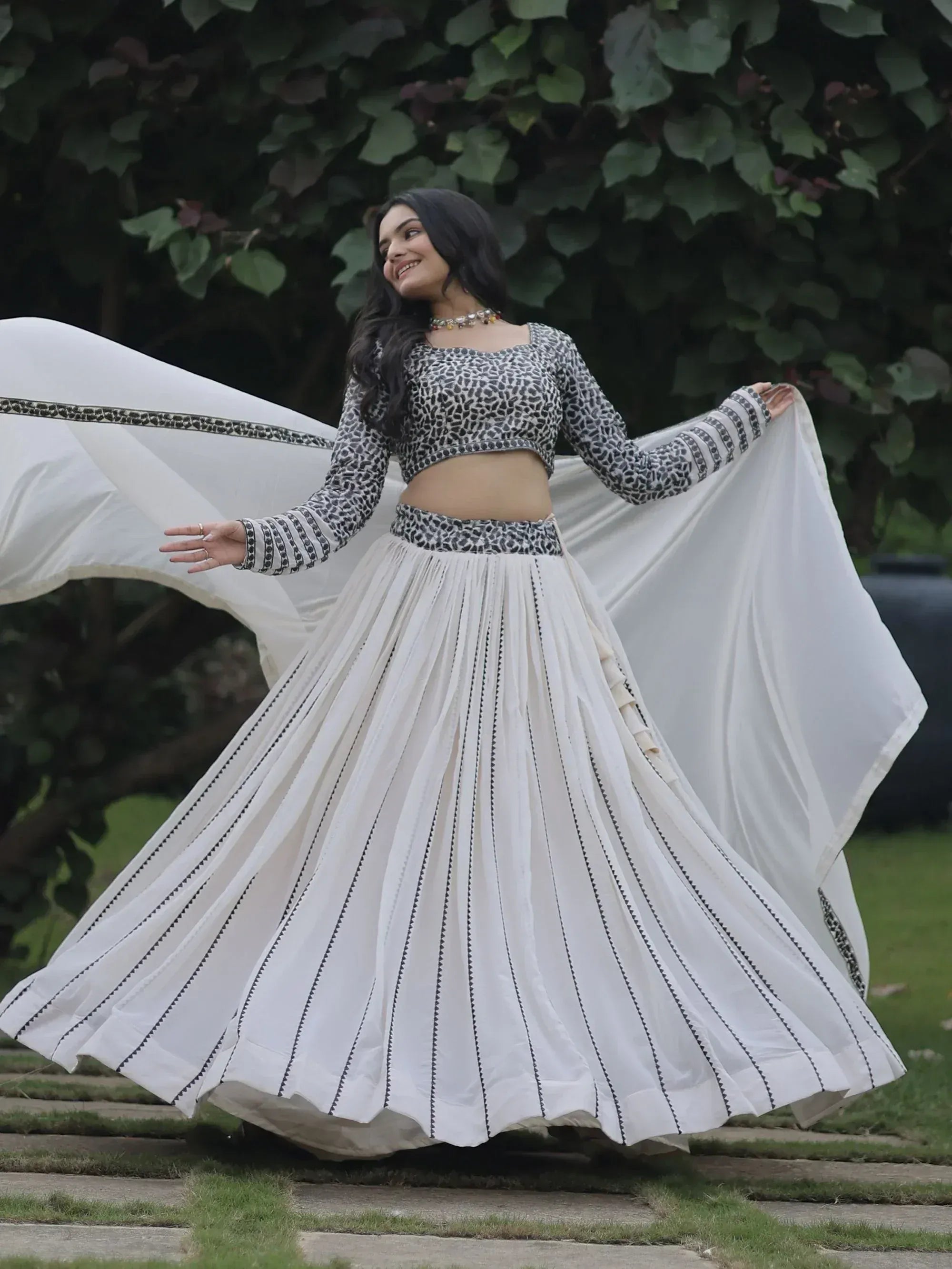 Woman in white pleated lehenga with black print crop top, twirling outdoors