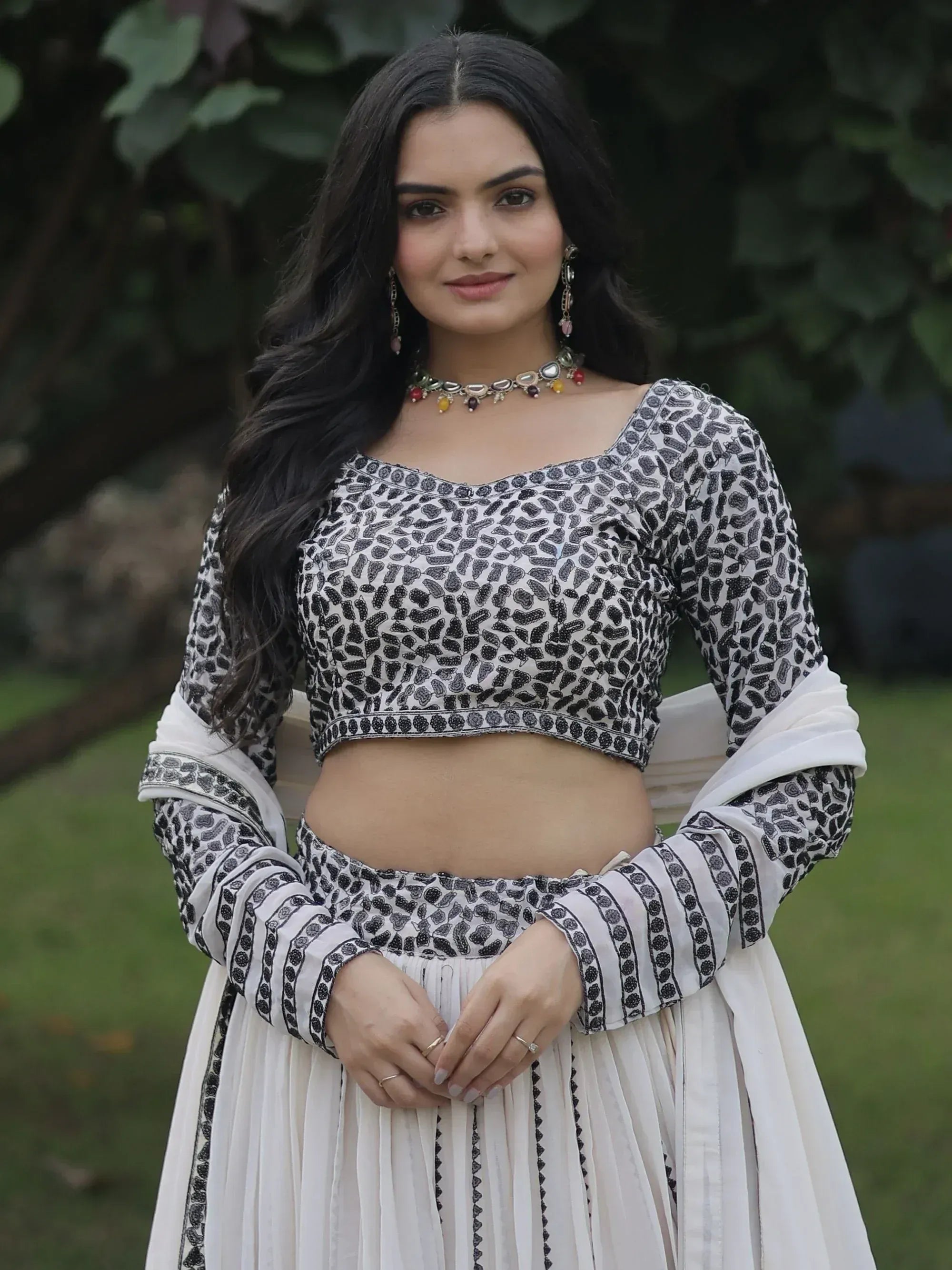 Woman in black and white printed ethnic crop top and pleated skirt, styled with traditional jewelry for festive occasions.