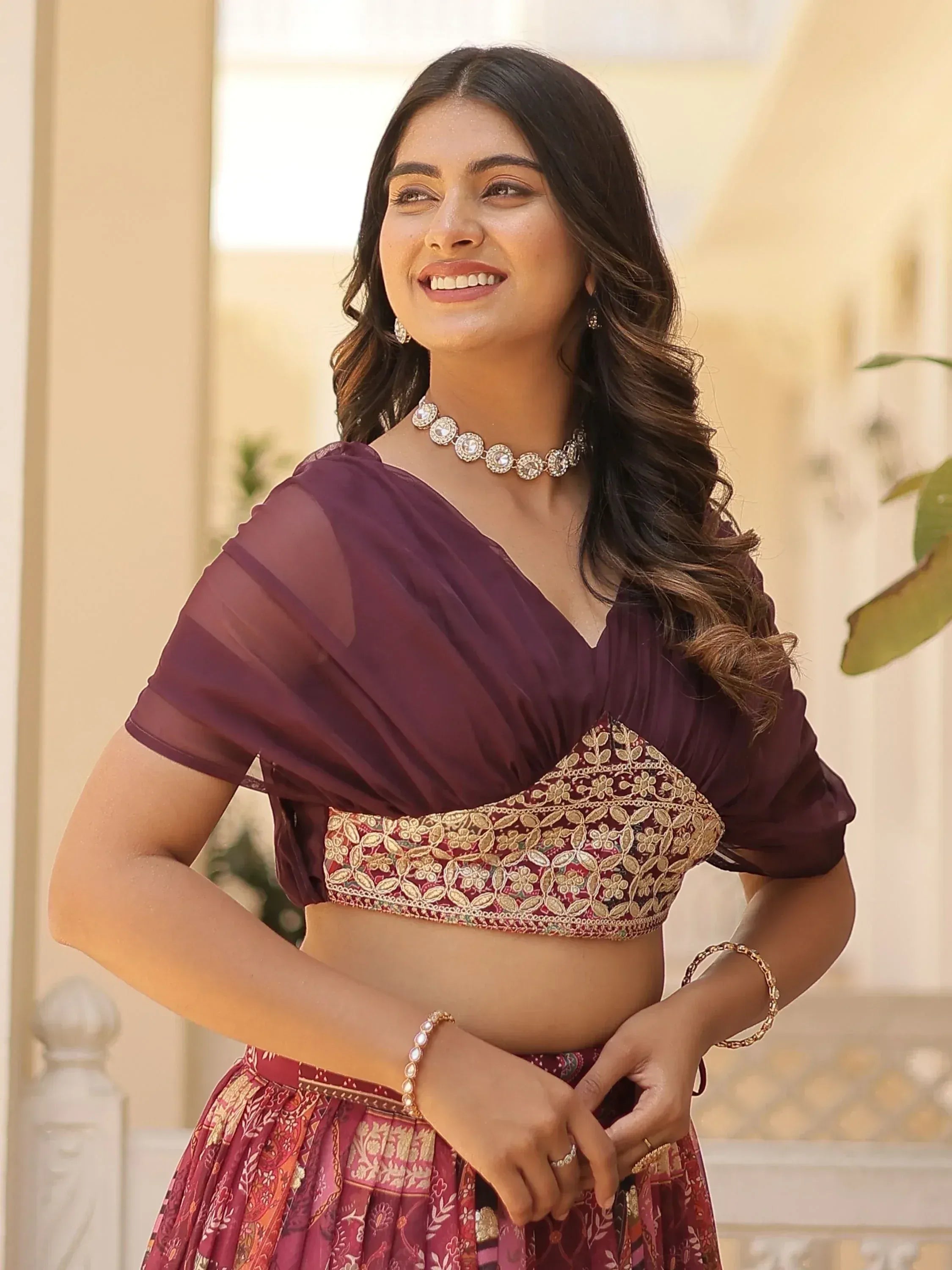 Woman in maroon embroidered lehenga choli with sheer dupatta, gold jewelry, smiling outdoors