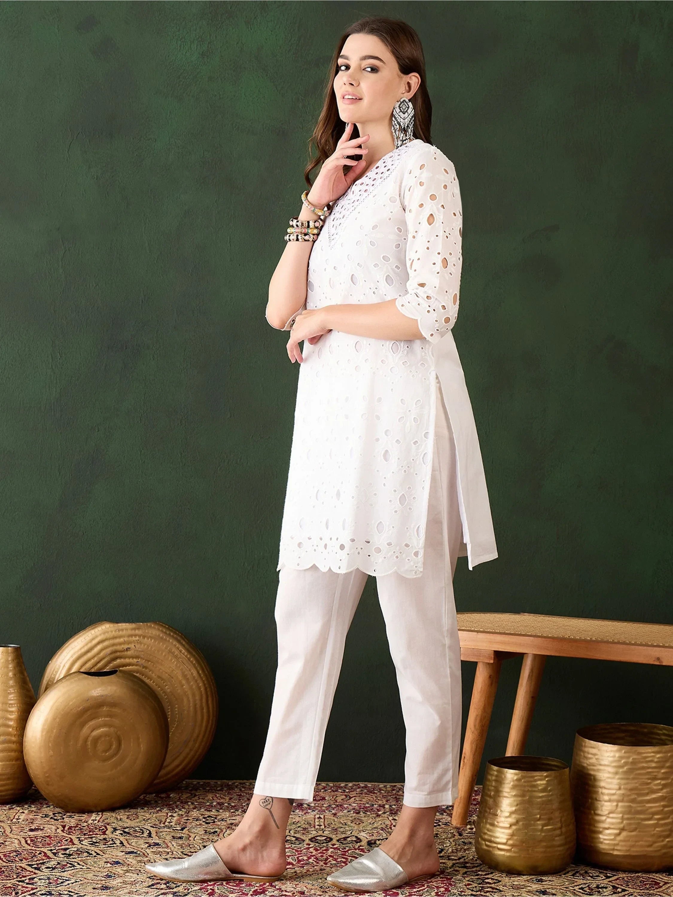 Woman wearing white embroidered kurta and pants, silver flats, ethnic jewelry, indoor setting