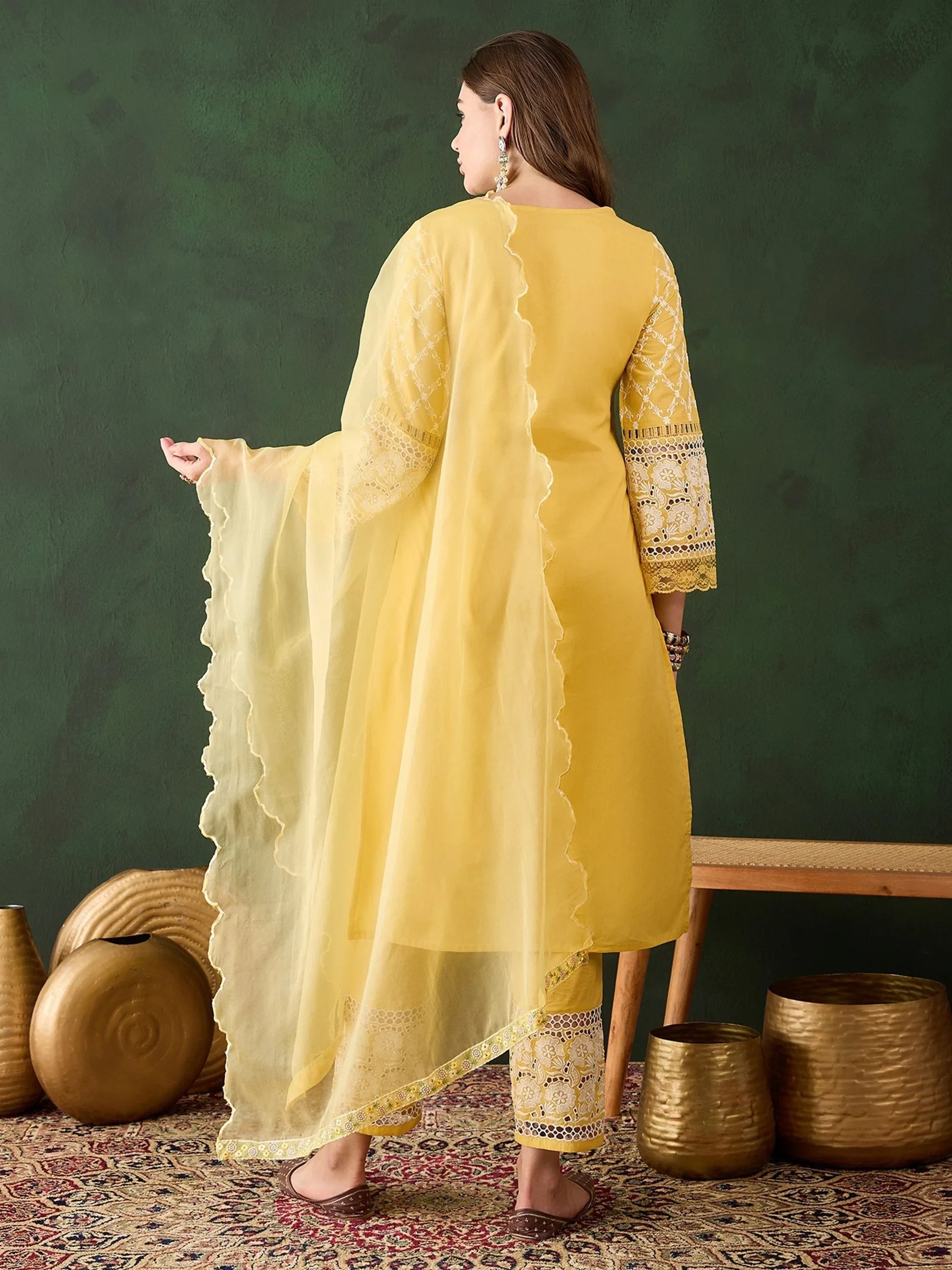 Woman in yellow embroidered salwar kameez and dupatta, standing on a patterned rug