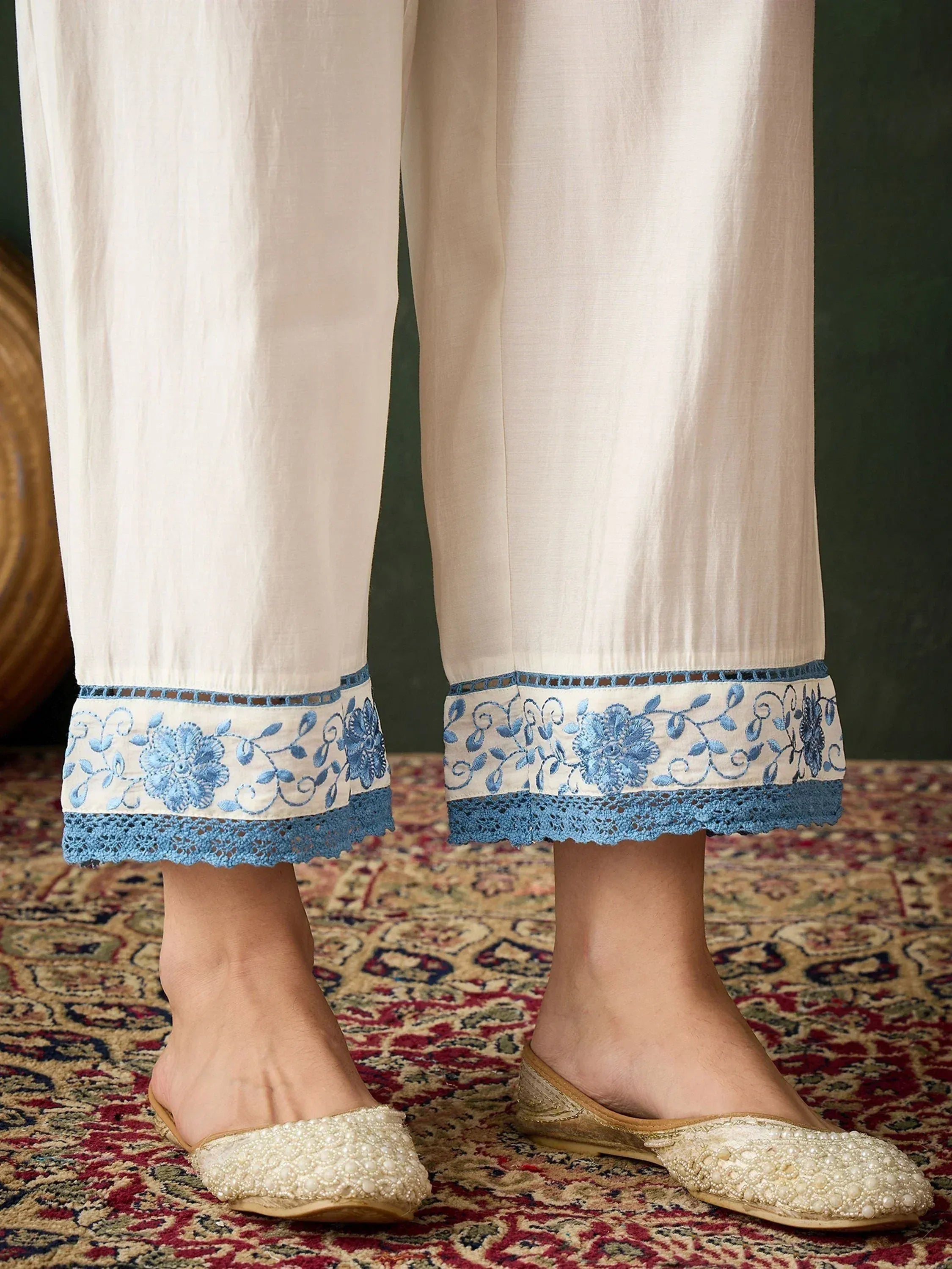 Cream palazzo pants with blue floral embroidery and lace hem, paired with pearl-embellished flats.