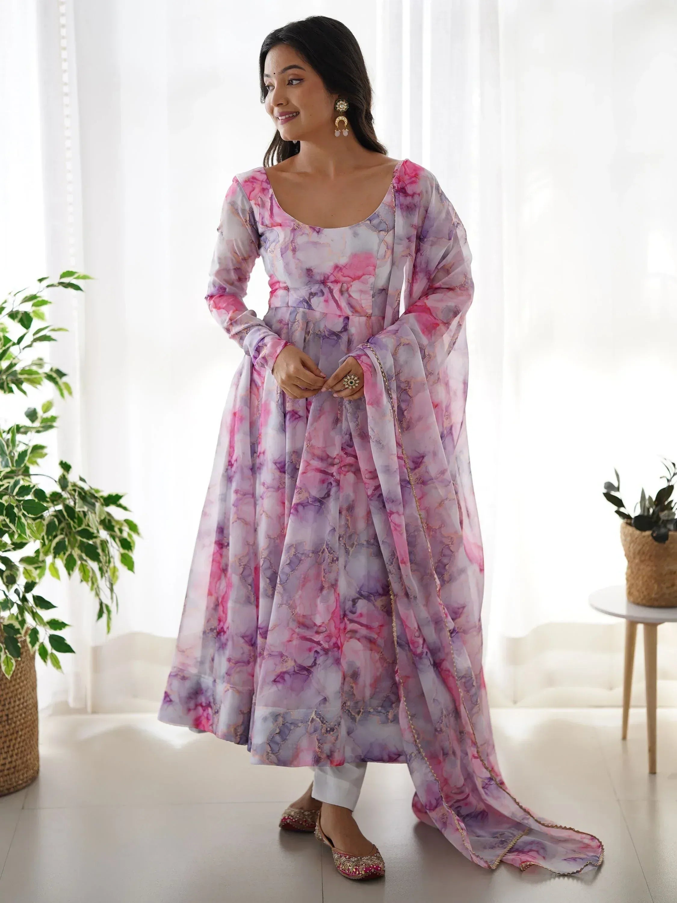 Pink and purple floral print ethnic gown with sheer sleeves and gold trim, paired with white pants and embellished flats.