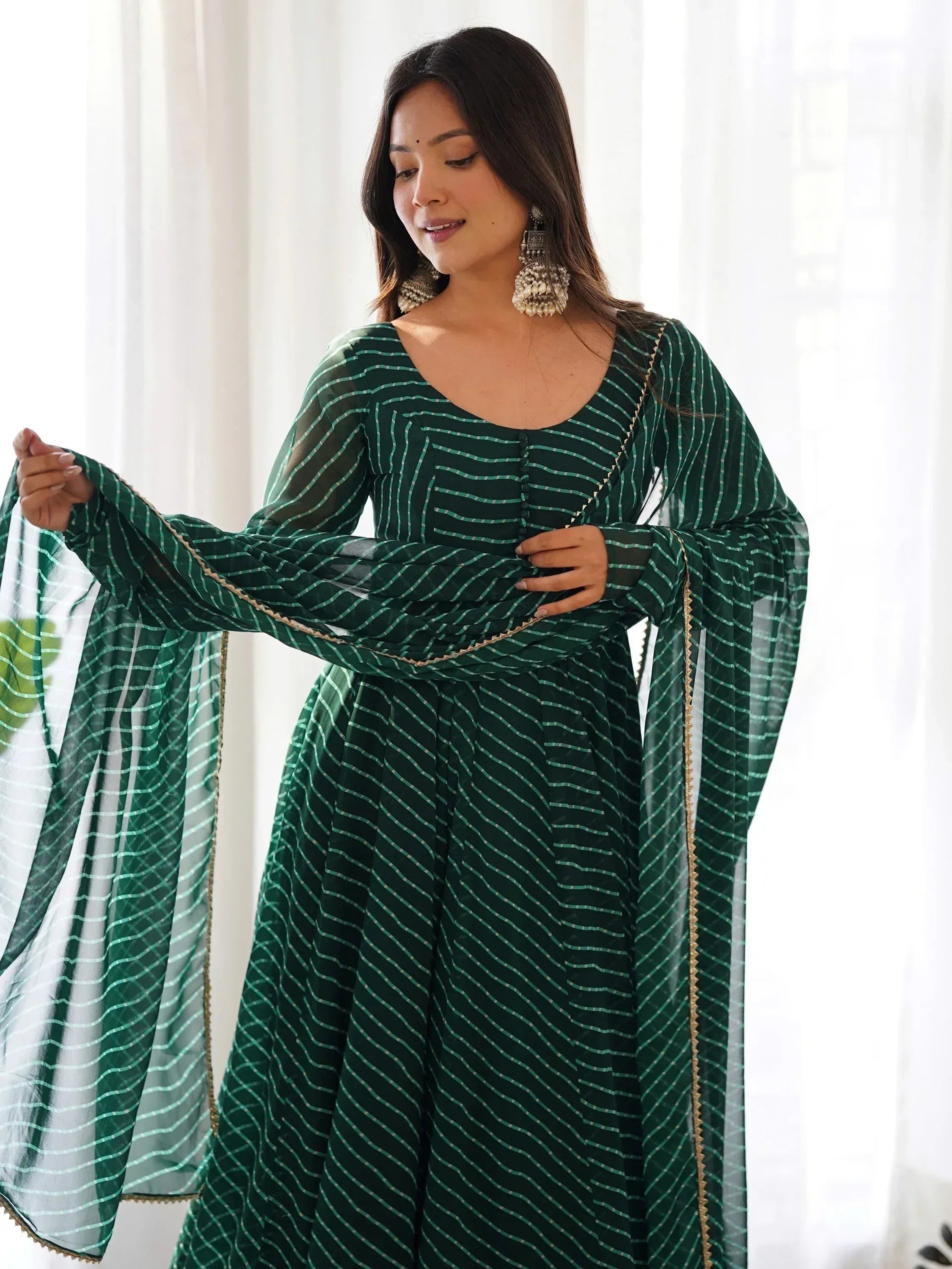 Emerald green striped ethnic gown with sheer sleeves and gold trim, styled with statement earrings.