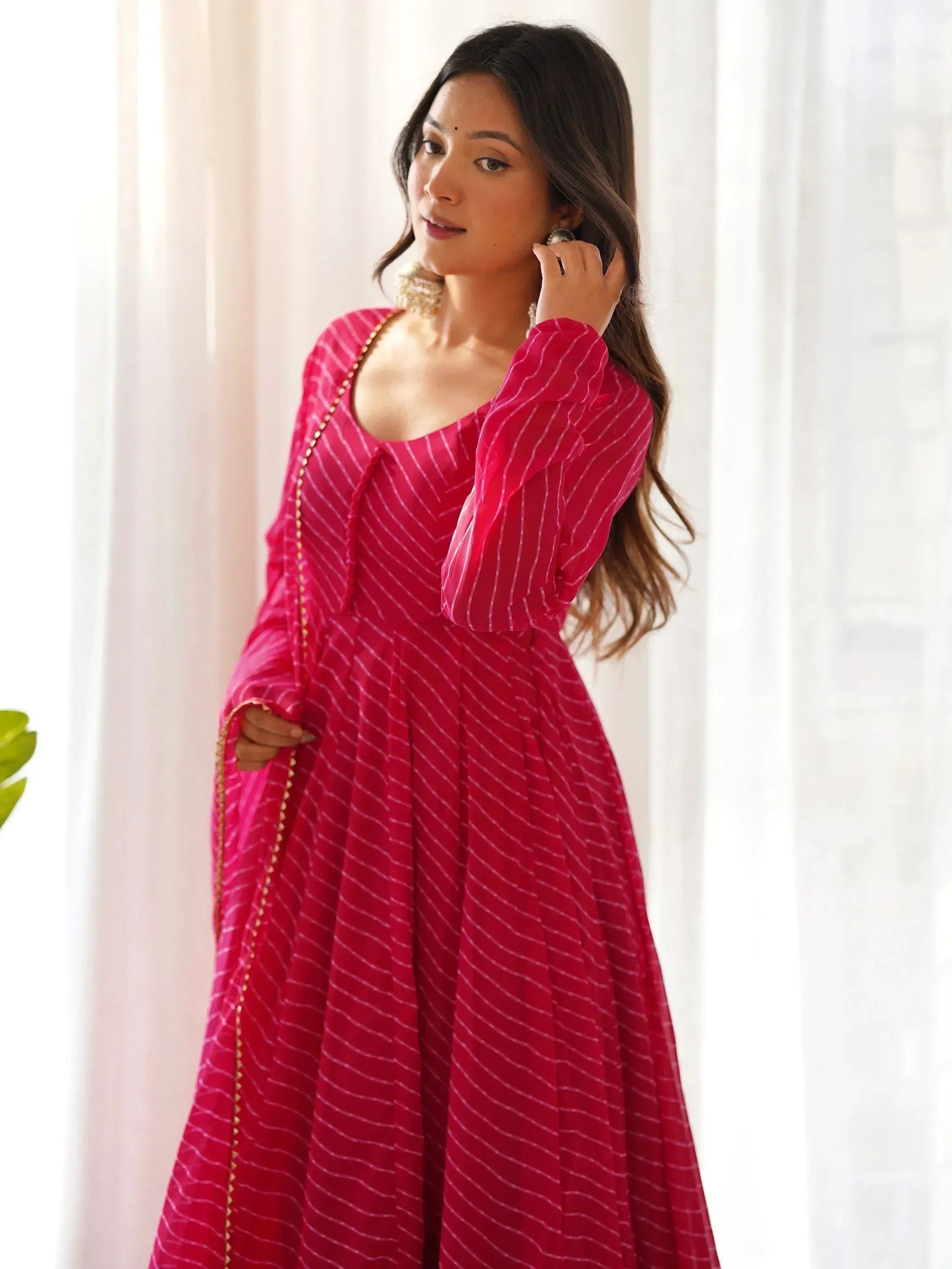 Woman in pink striped ethnic gown with gold trim, stylish Indian wear for festive occasions