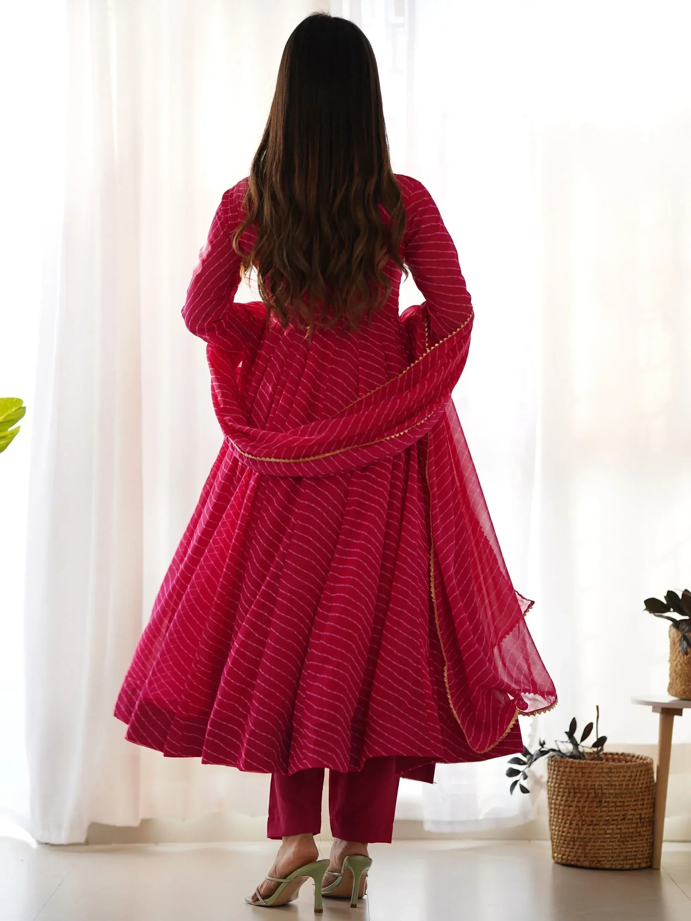 Woman in red striped ethnic anarkali suit with gold trim, back view, indoor setting