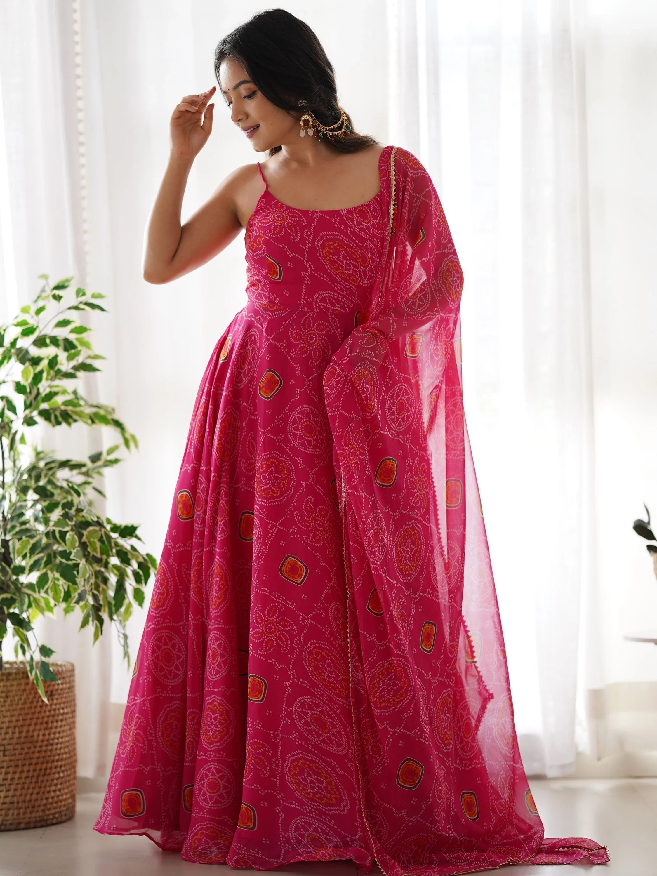 Woman wearing a vibrant pink bandhani print ethnic gown with dupatta indoors