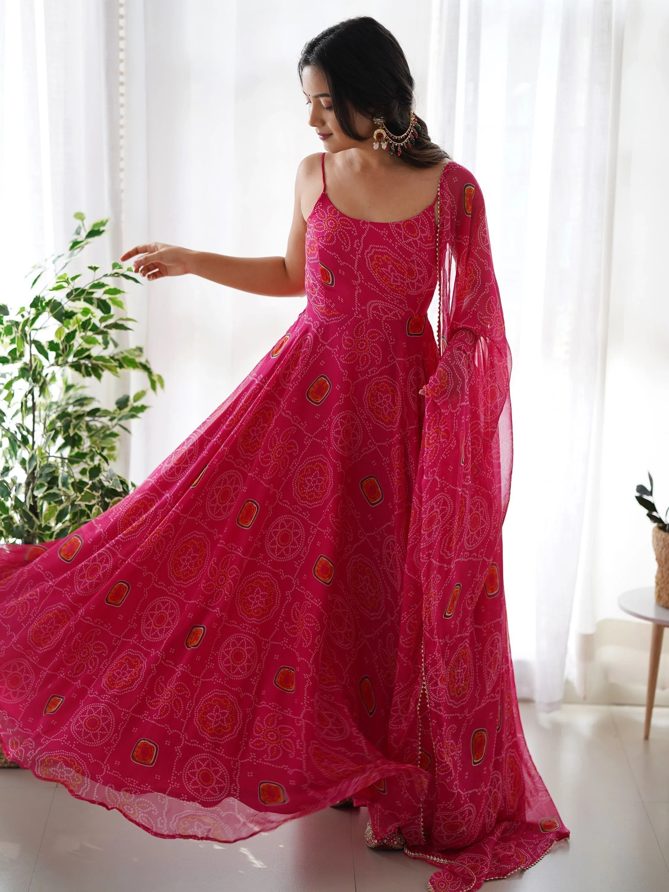 Woman in bright pink bandhani print ethnic gown with dupatta, standing indoors