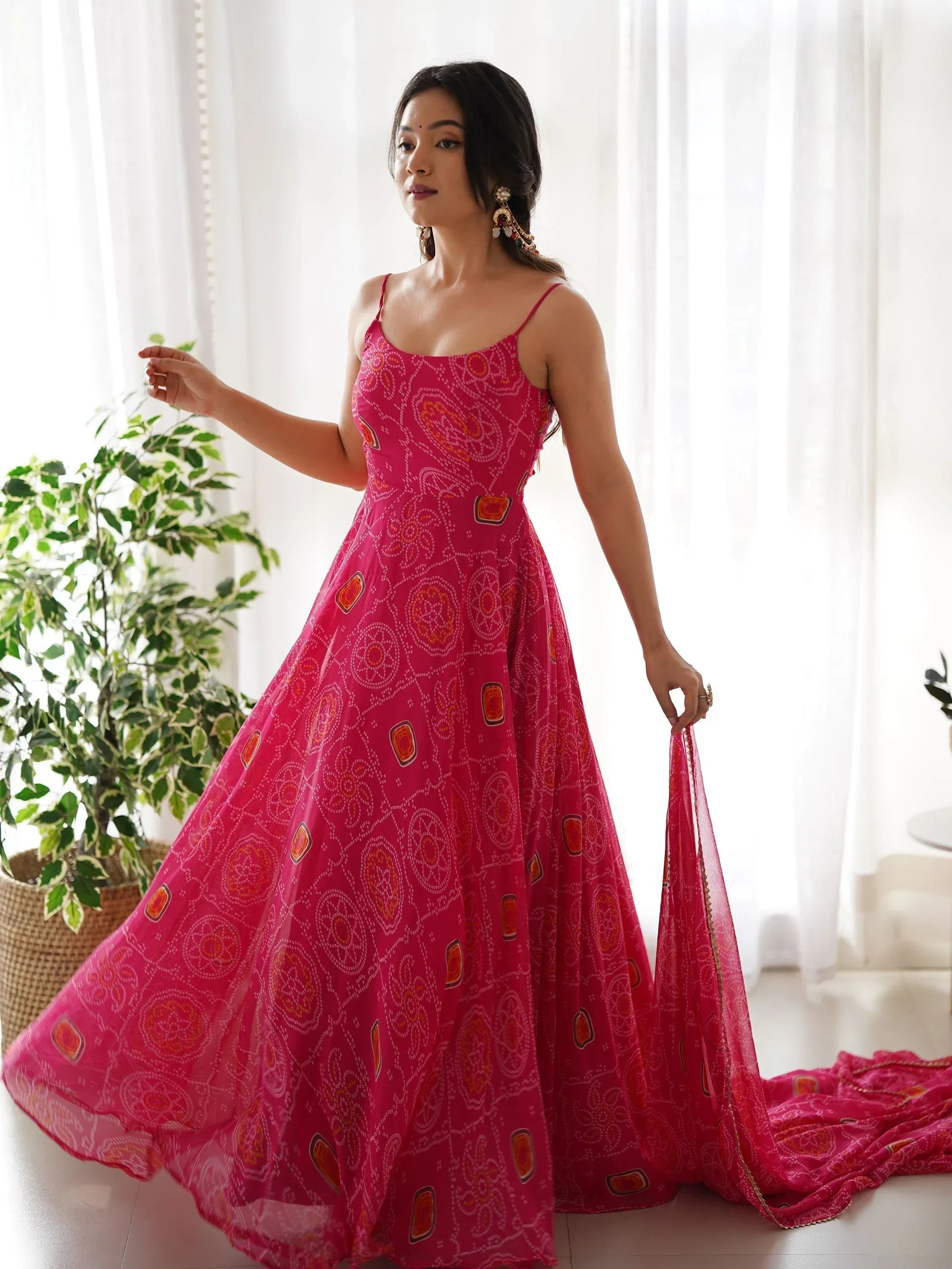 Woman in a pink Bandhani printed ethnic gown with spaghetti straps in a bright indoor setting