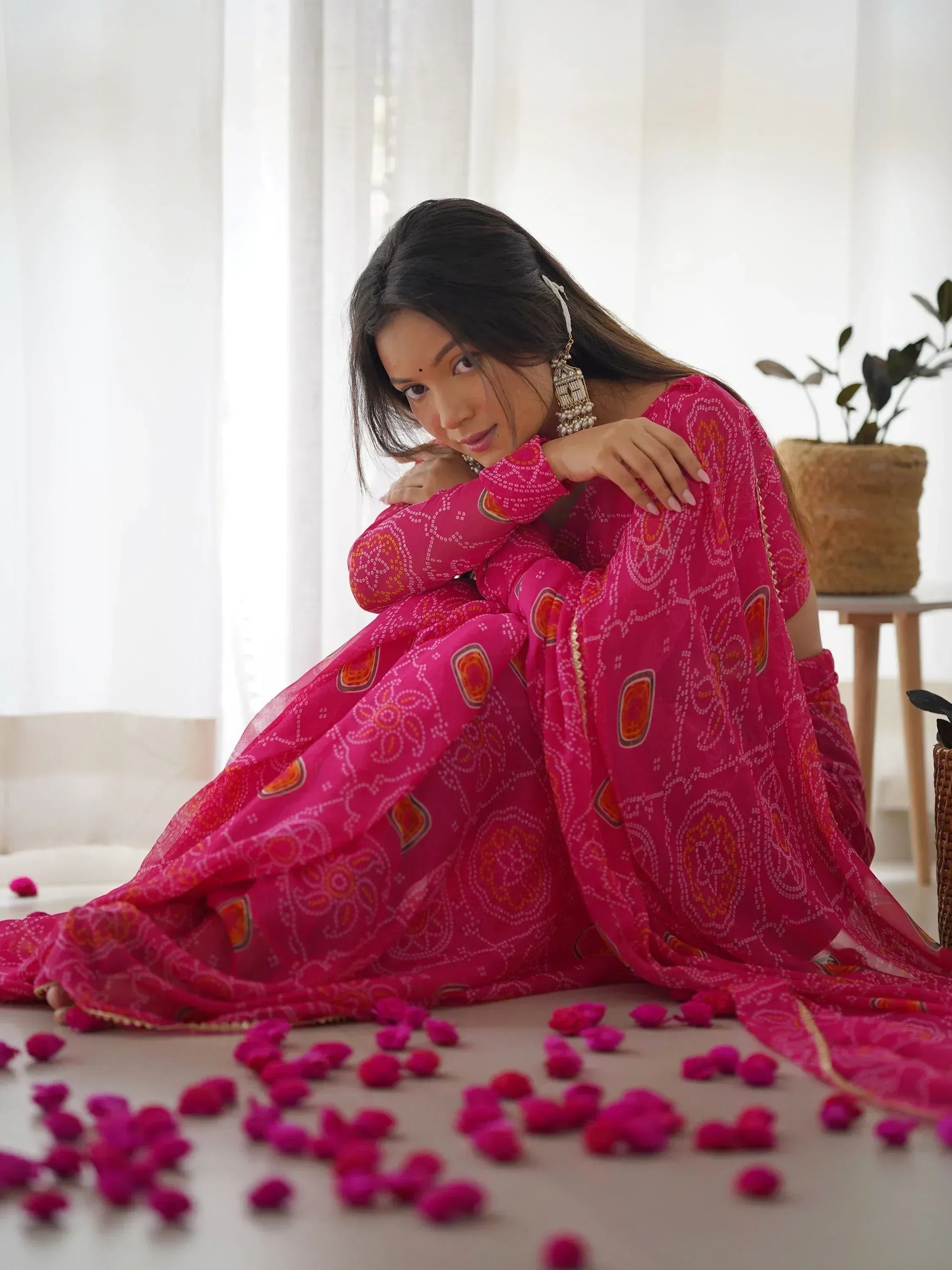 Woman in vibrant pink ethnic gown with bandhani print, styled with jhumka earrings and rose petals