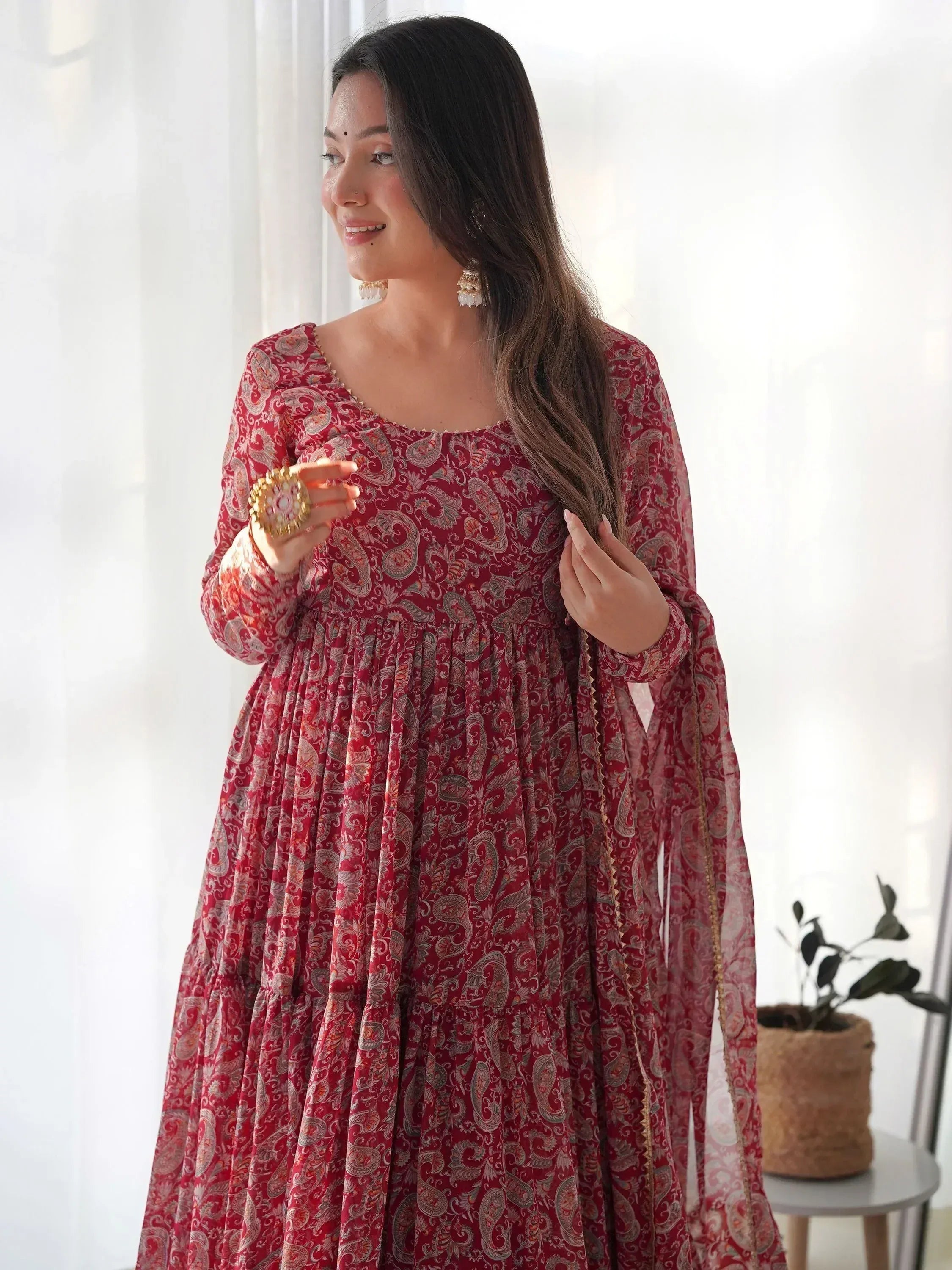 Woman in red paisley print ethnic gown with gold trim, styled with traditional jewelry for festive occasions