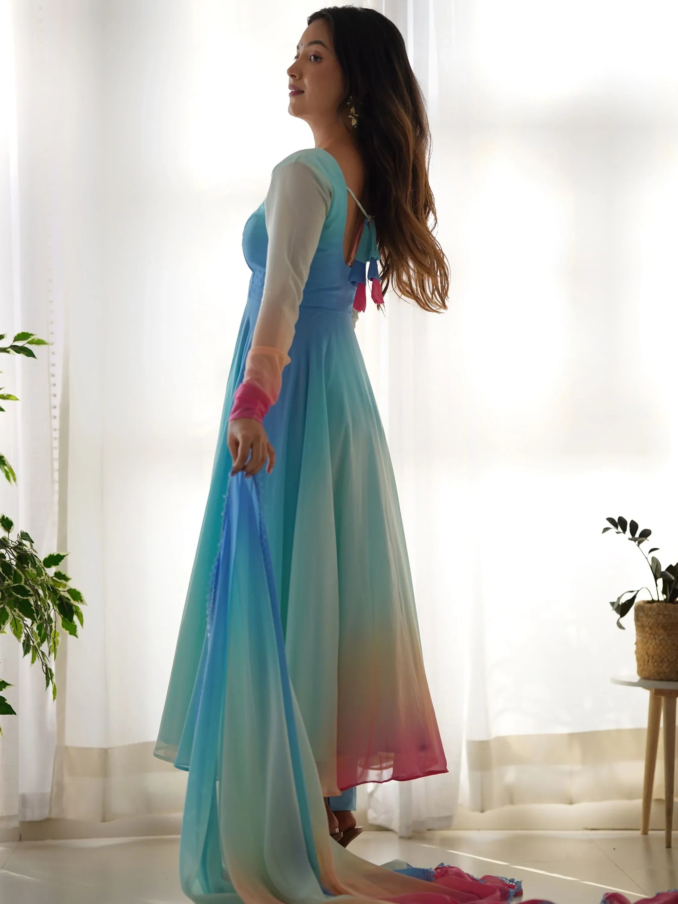 Woman in pastel blue ombre ethnic gown with sheer sleeves and dupatta, indoors by window