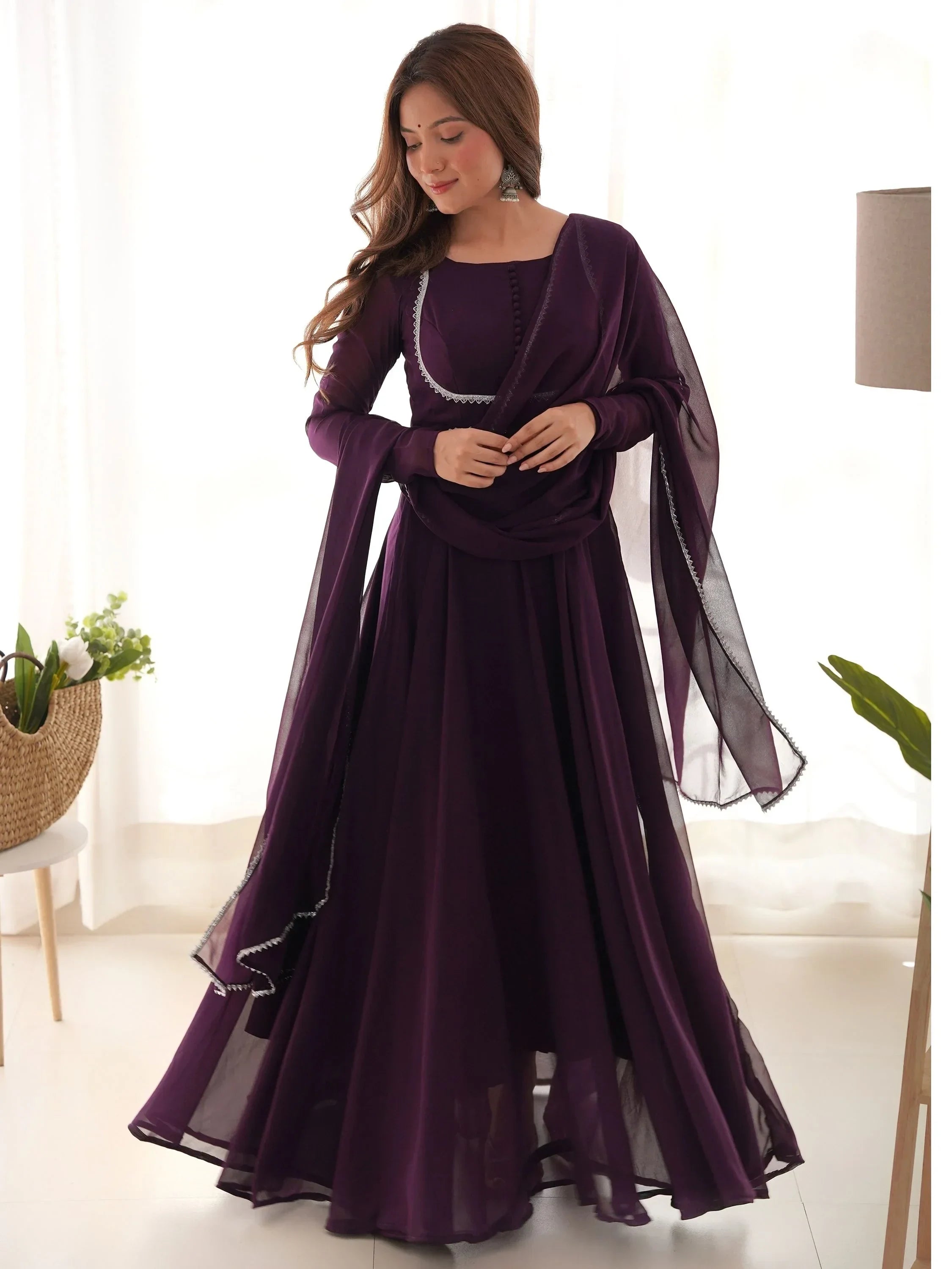 Woman in a purple ethnic gown with dupatta, posing indoors in natural light