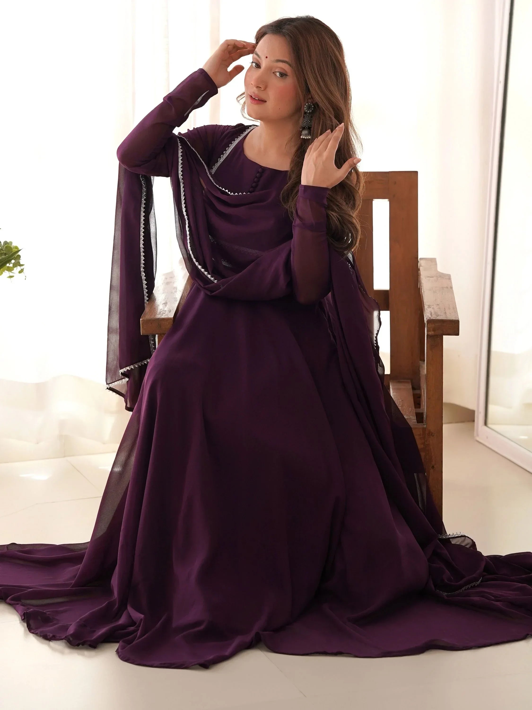 Woman in a purple anarkali suit with dupatta, sitting on a wooden bench indoors