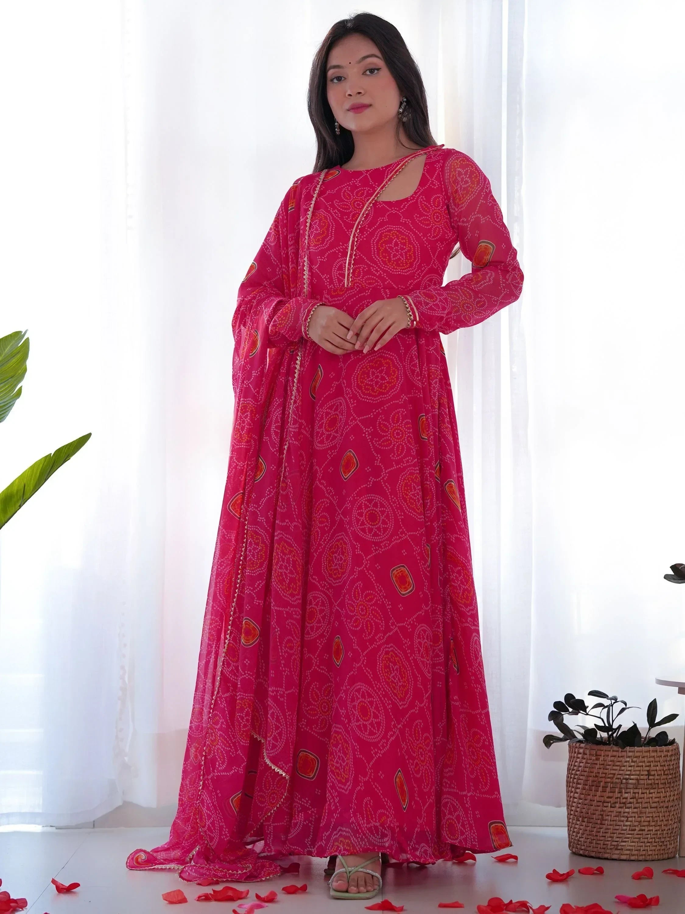 Woman wearing a vibrant pink ethnic gown with traditional print and dupatta indoors