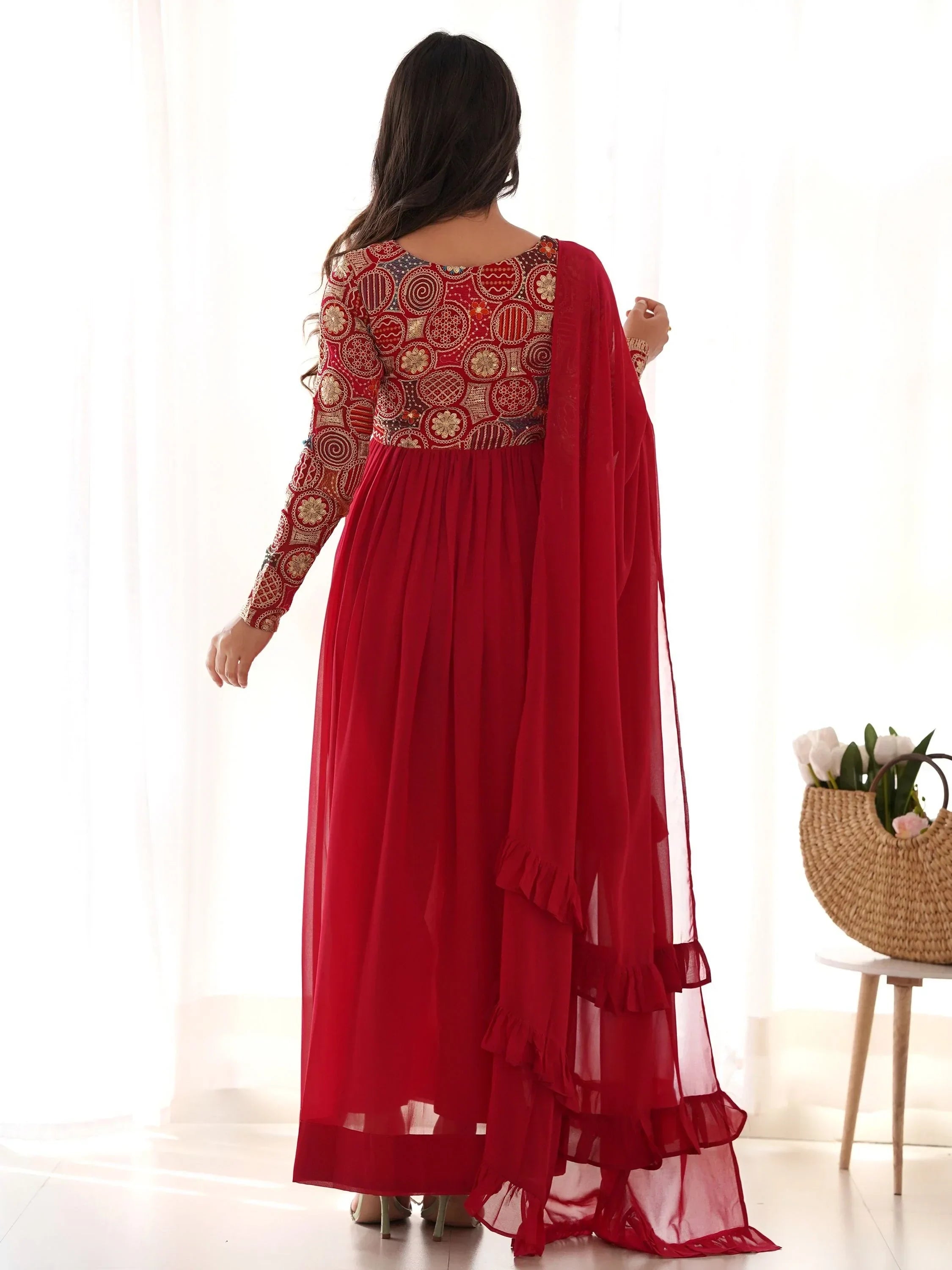 Woman wearing a red embroidered Anarkali suit with dupatta, standing indoors
