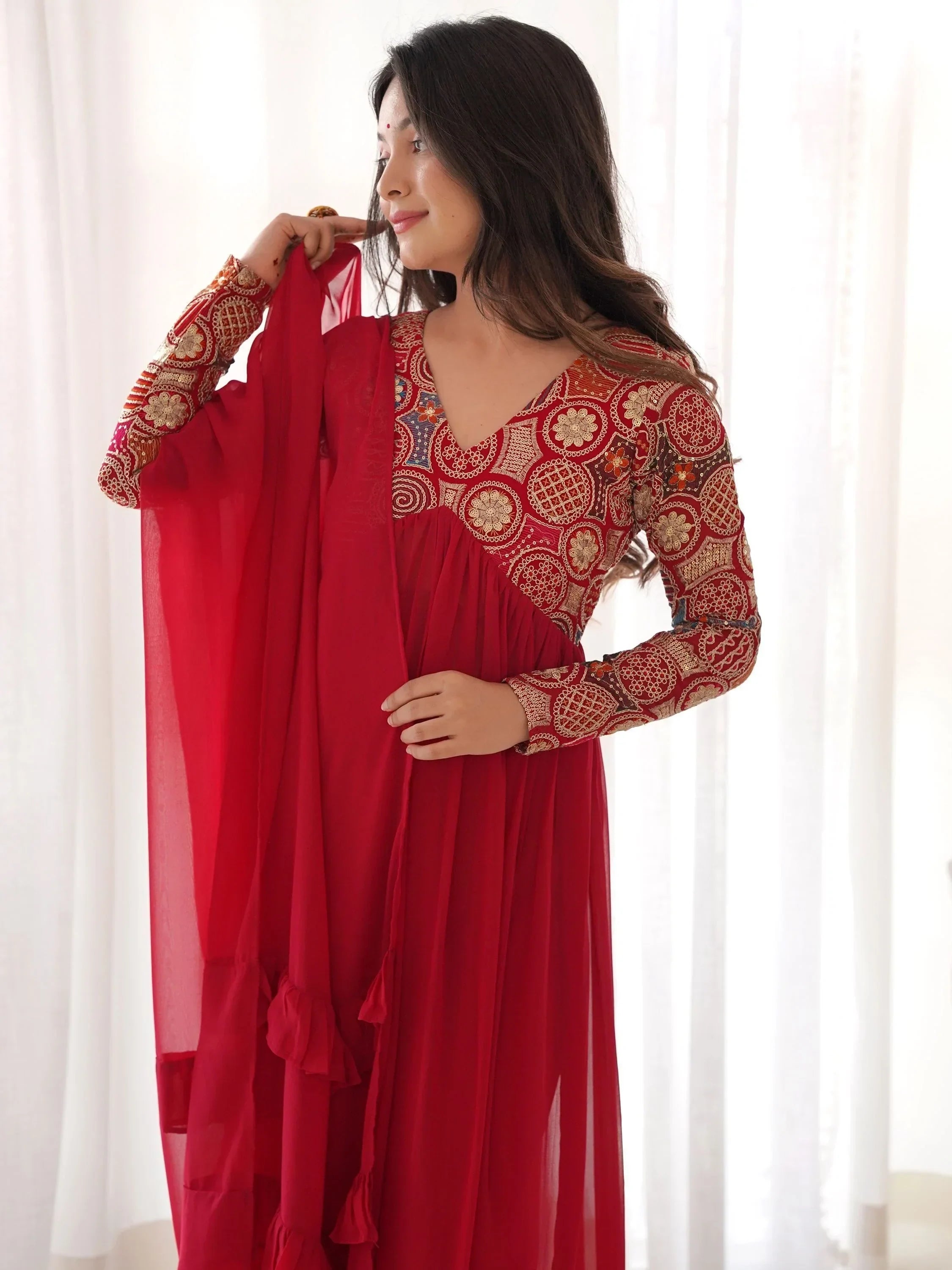 Woman wearing red embroidered Indian ethnic gown with dupatta, standing indoors