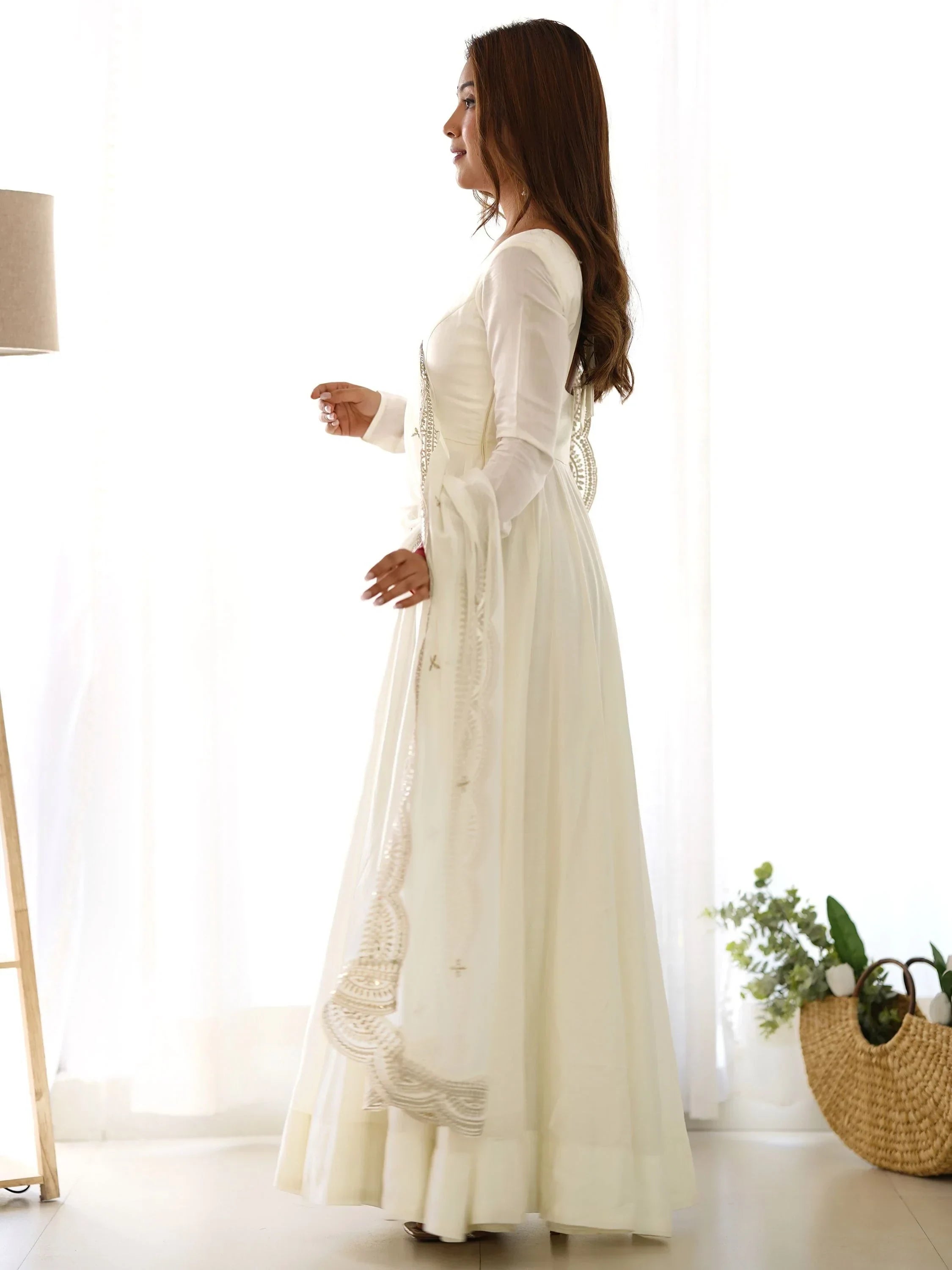 Woman in white embroidered ethnic gown with dupatta standing indoors