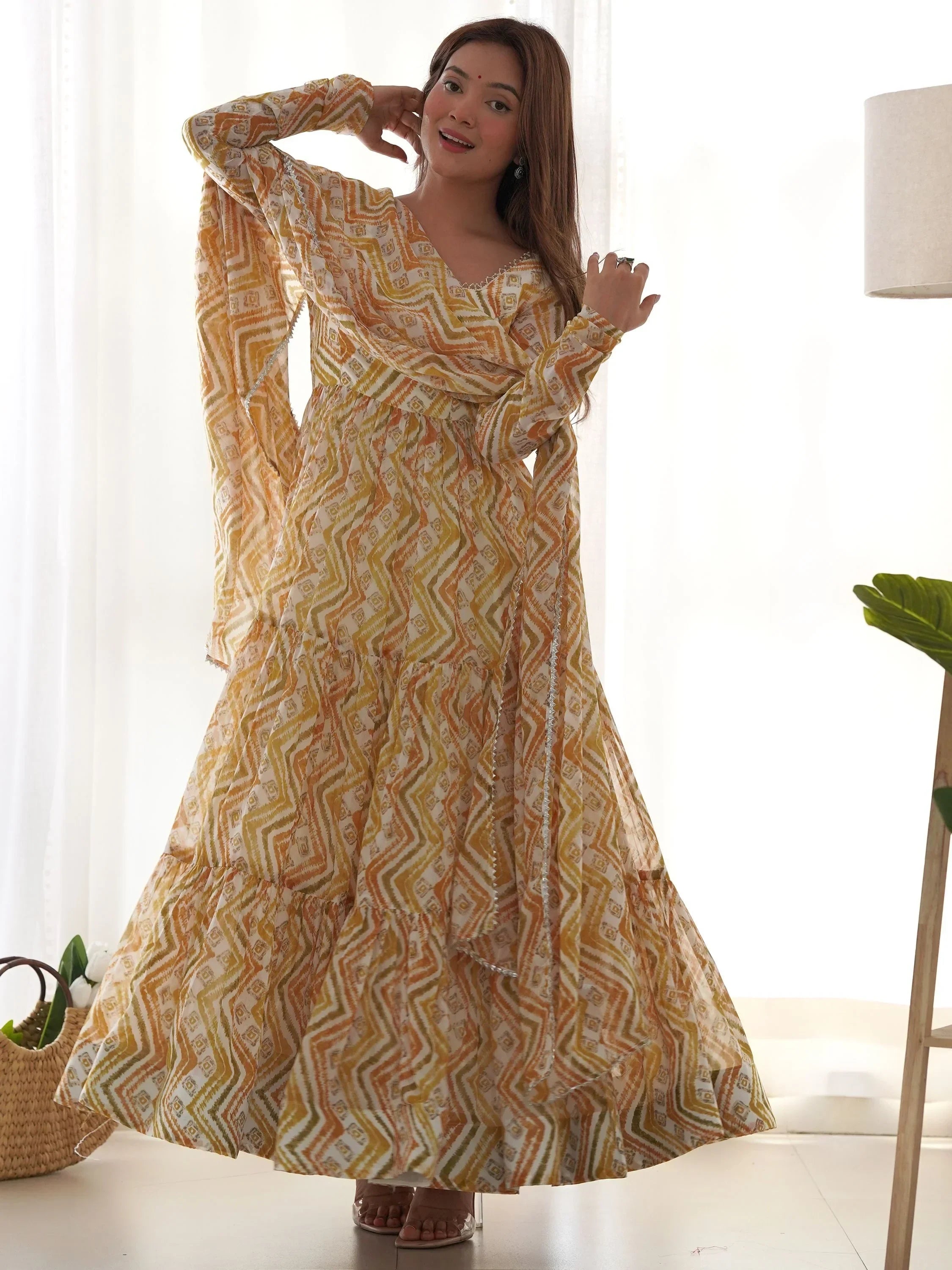 Woman in yellow printed ethnic gown with dupatta, standing indoors