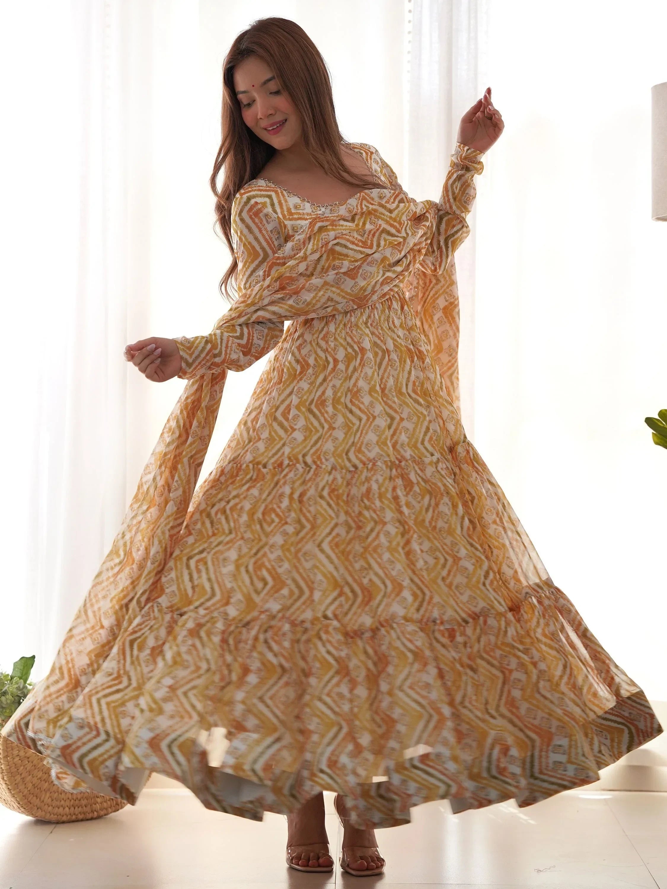 Woman in a flowing printed yellow and white ethnic gown dancing indoors