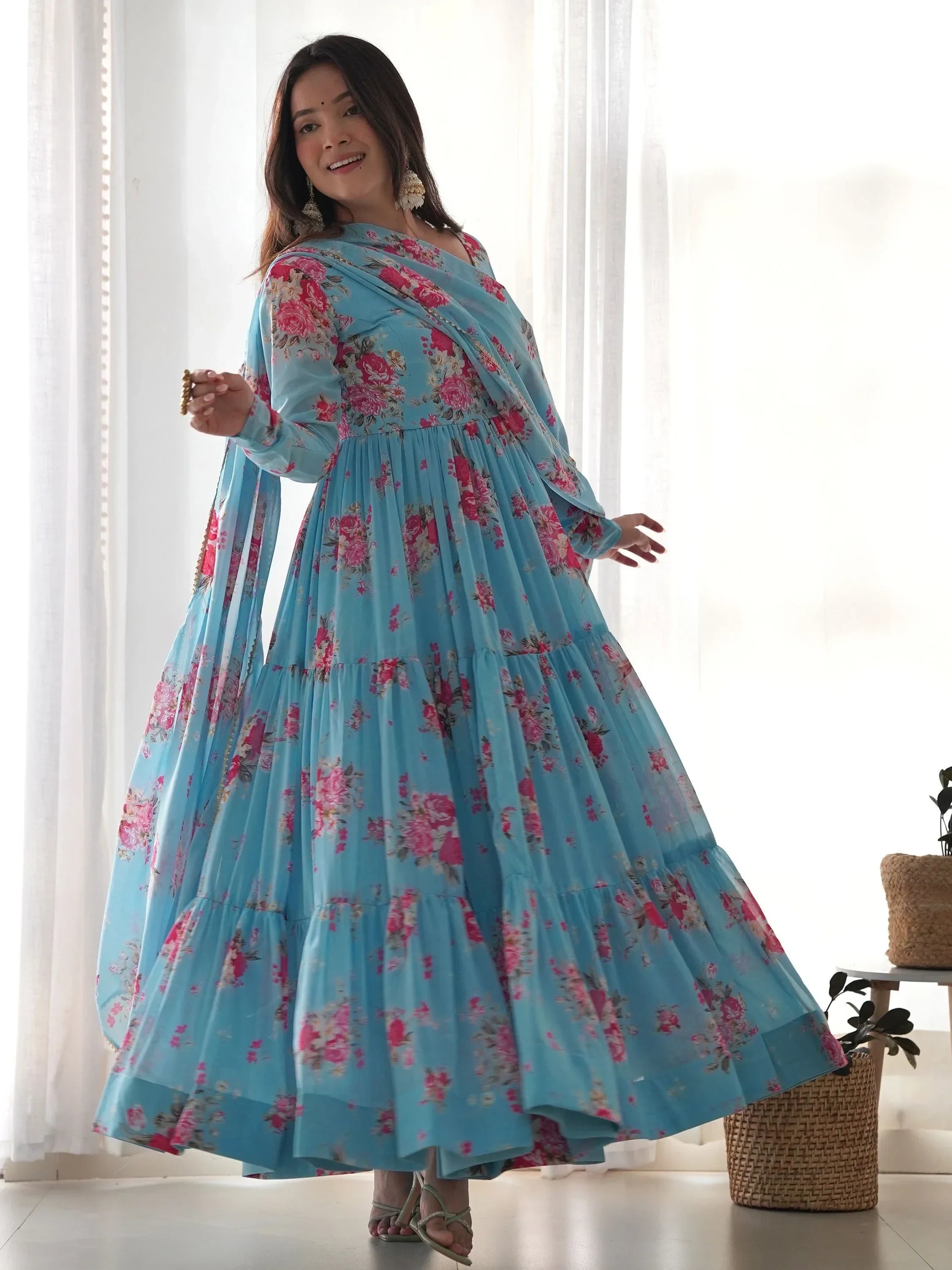 Woman wearing a blue floral print Anarkali gown with dupatta, standing indoors
