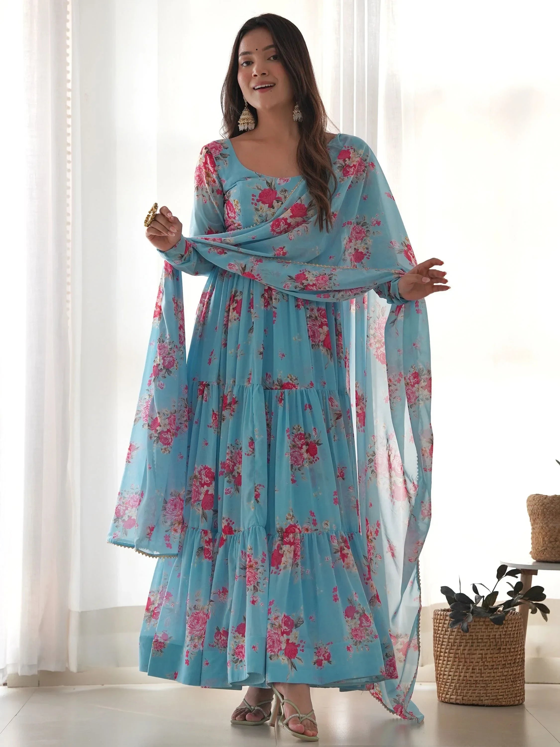 Woman wearing light blue floral ethnic gown with dupatta, standing indoors
