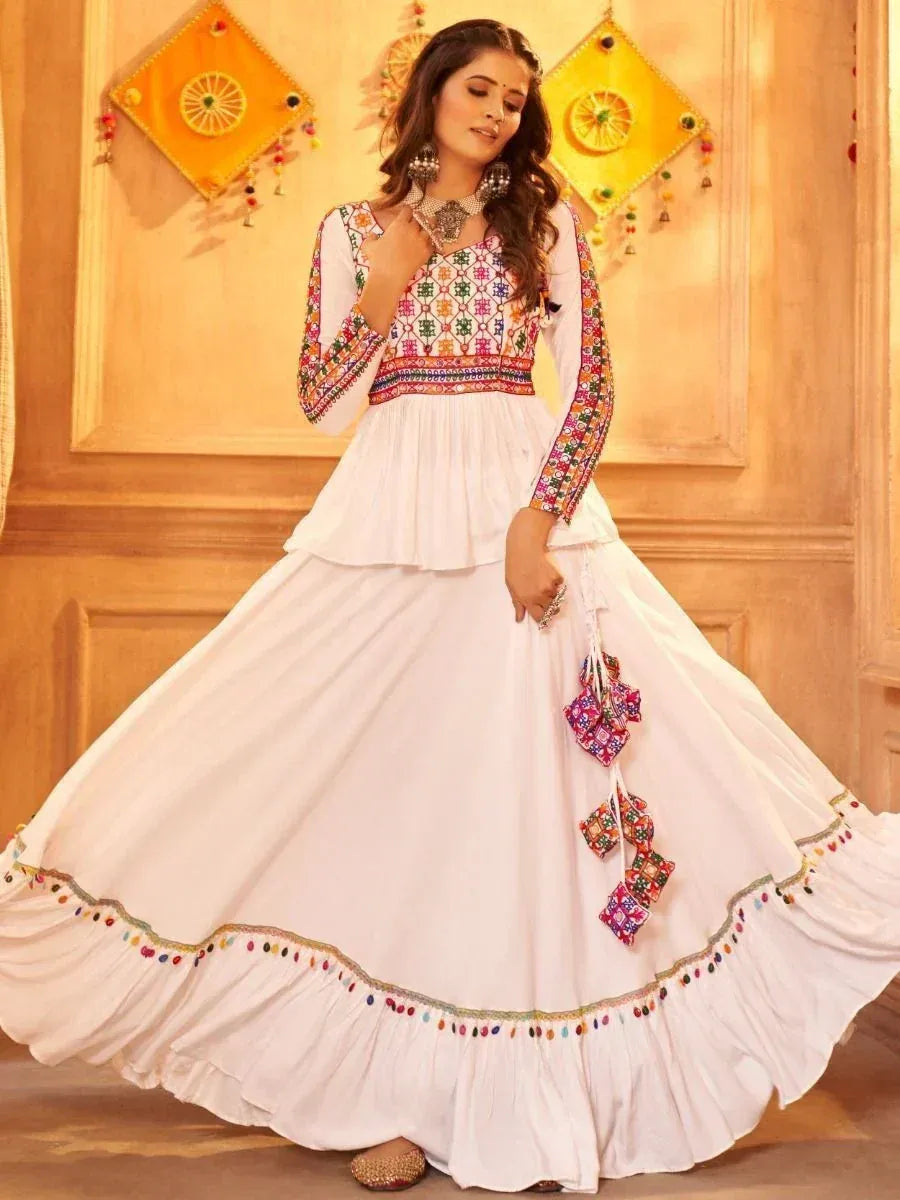 White embroidered ethnic gown with colorful mirror work and tassels, perfect for Indian celebrations