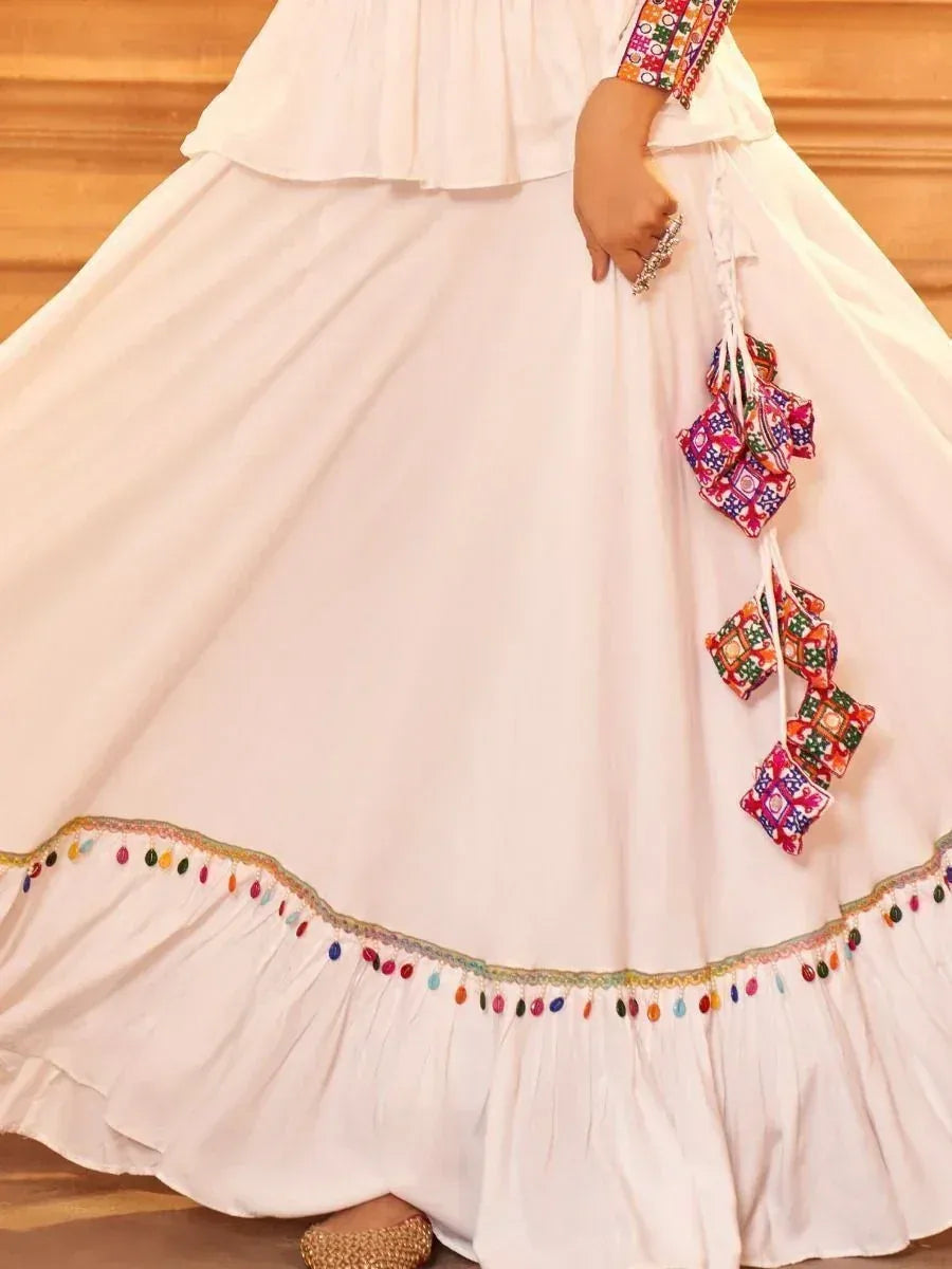 White ethnic gown with colorful mirror work and tassel detailing, perfect for Indian festive occasions