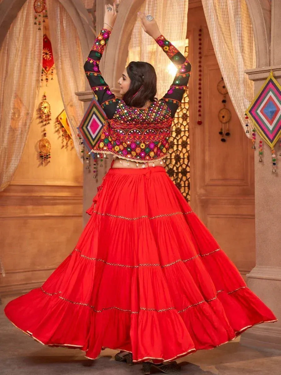 Woman in vibrant red tiered lehenga with colorful embroidered blouse, dancing in traditional Indian setting