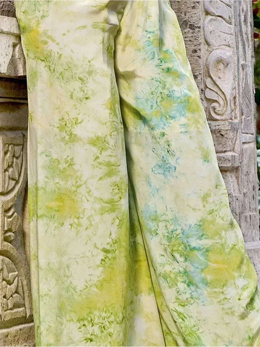 Green and blue tie-dye ethnic gown fabric draped on carved stone, perfect for designer Indian wear