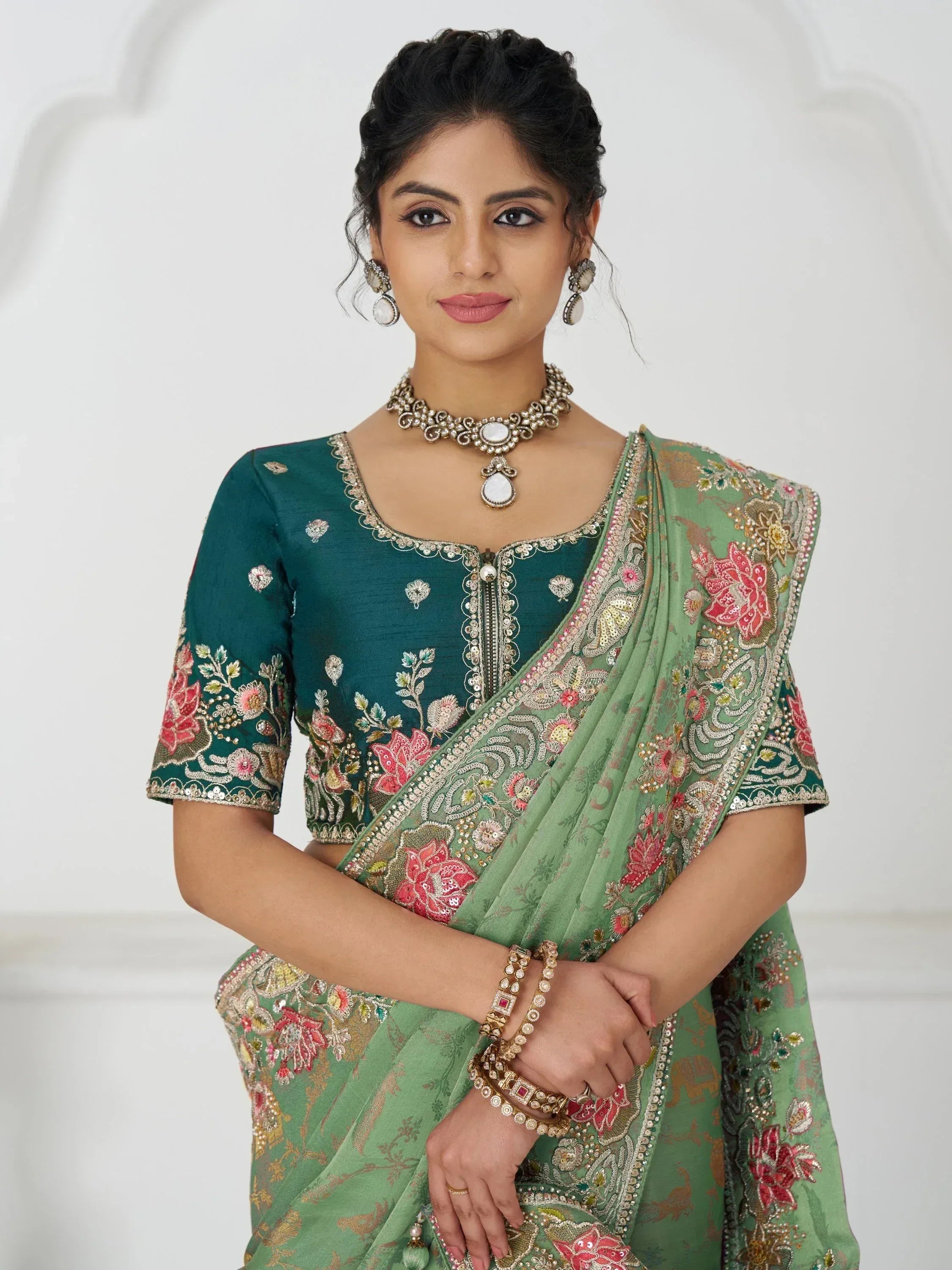 Woman in green embroidered saree with floral designs, matching blouse, and traditional jewelry