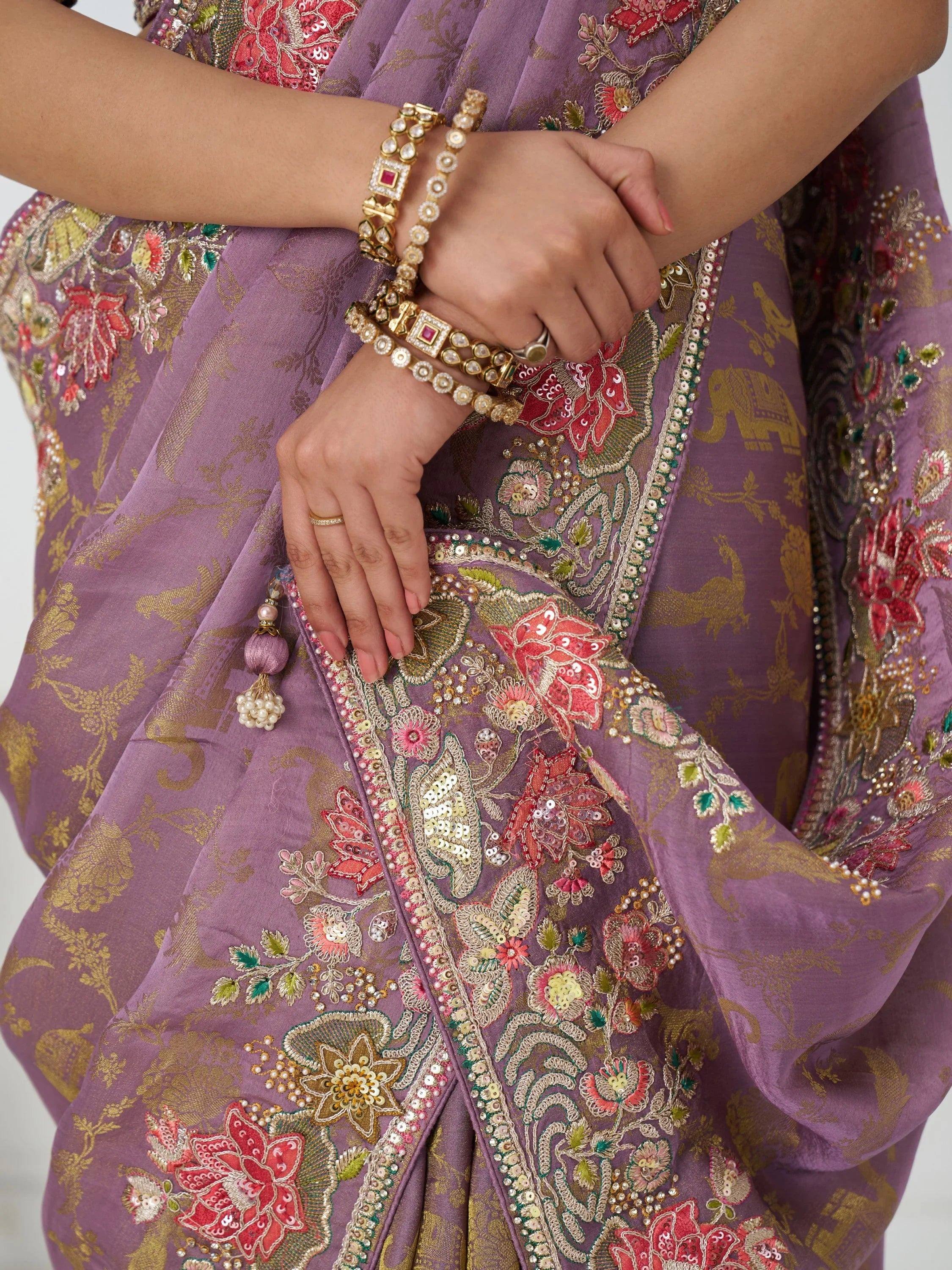 Purple embroidered saree with floral and elephant motifs, paired with gold jewelry