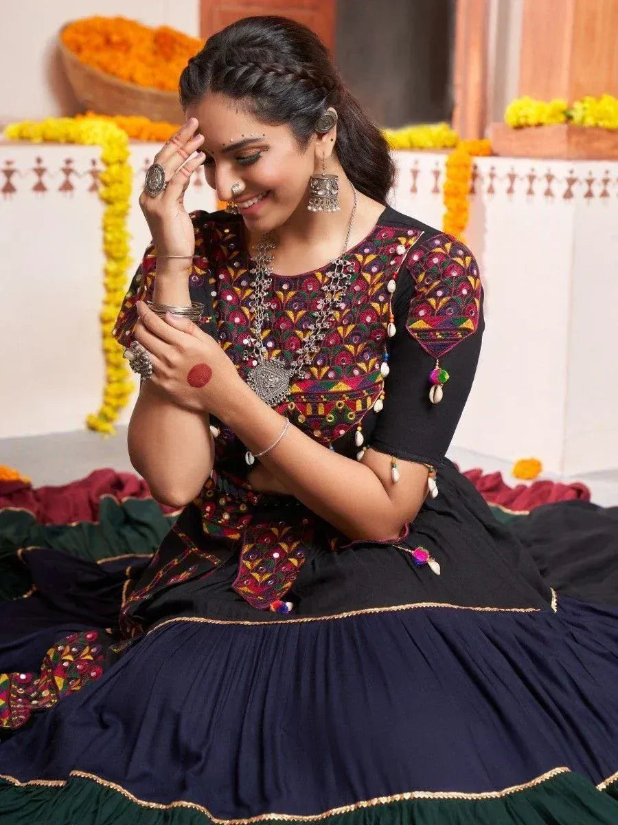 Woman in black embroidered ethnic gown with colorful mirror work, traditional jewelry, and marigold decor