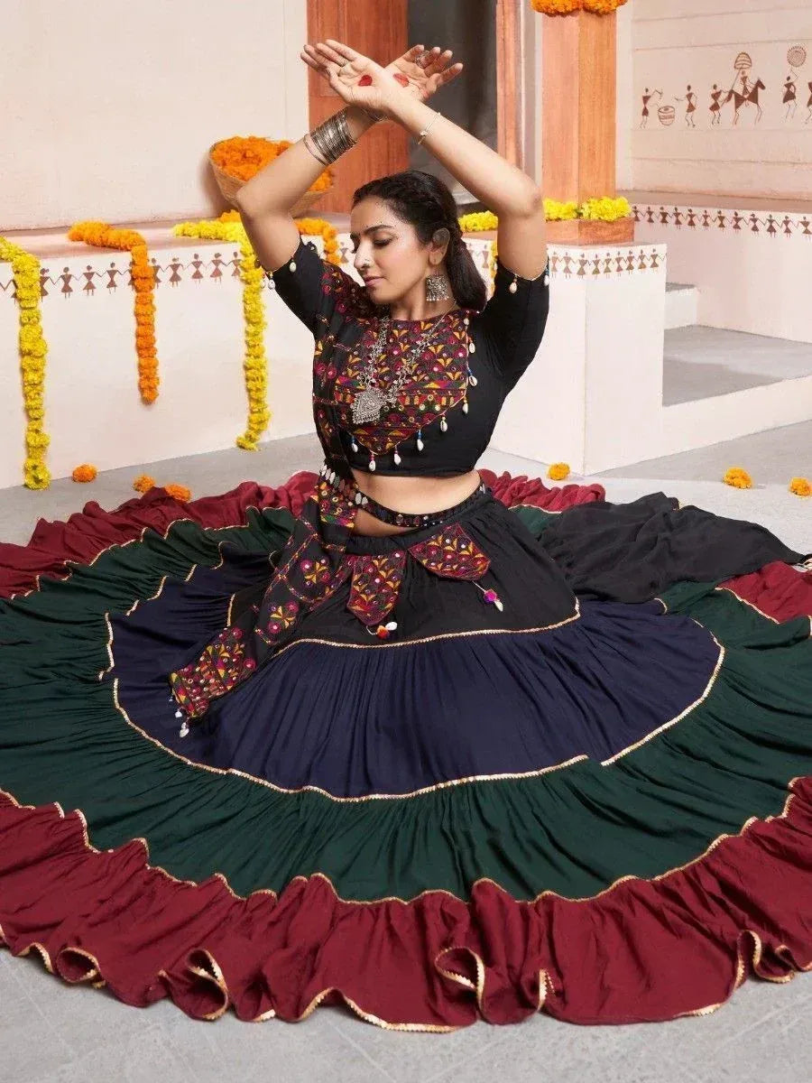 Woman in embroidered black and maroon lehenga choli, performing traditional dance with floral decor