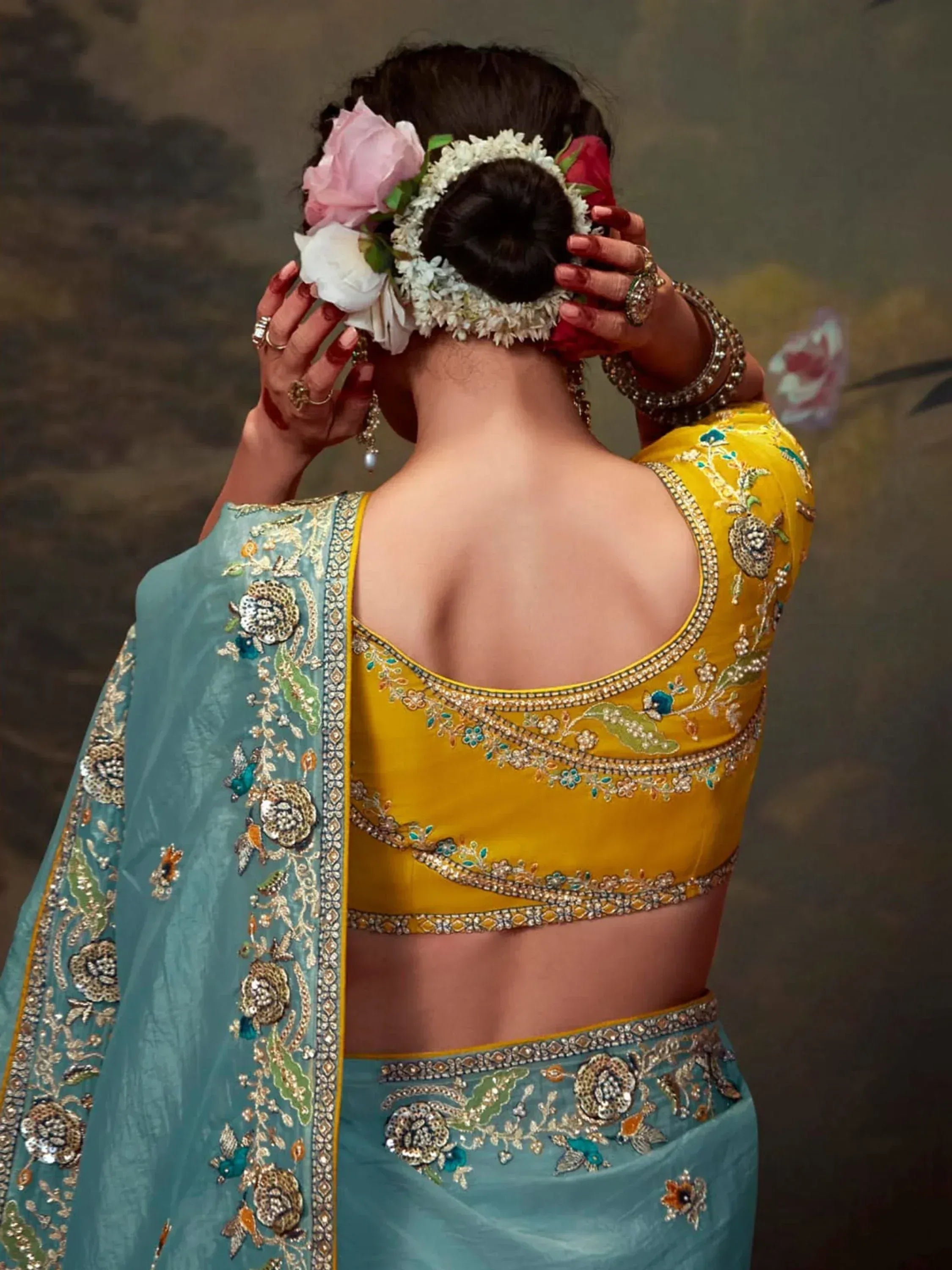 Back view of woman in yellow embroidered blouse and teal lehenga with floral hair accessories
