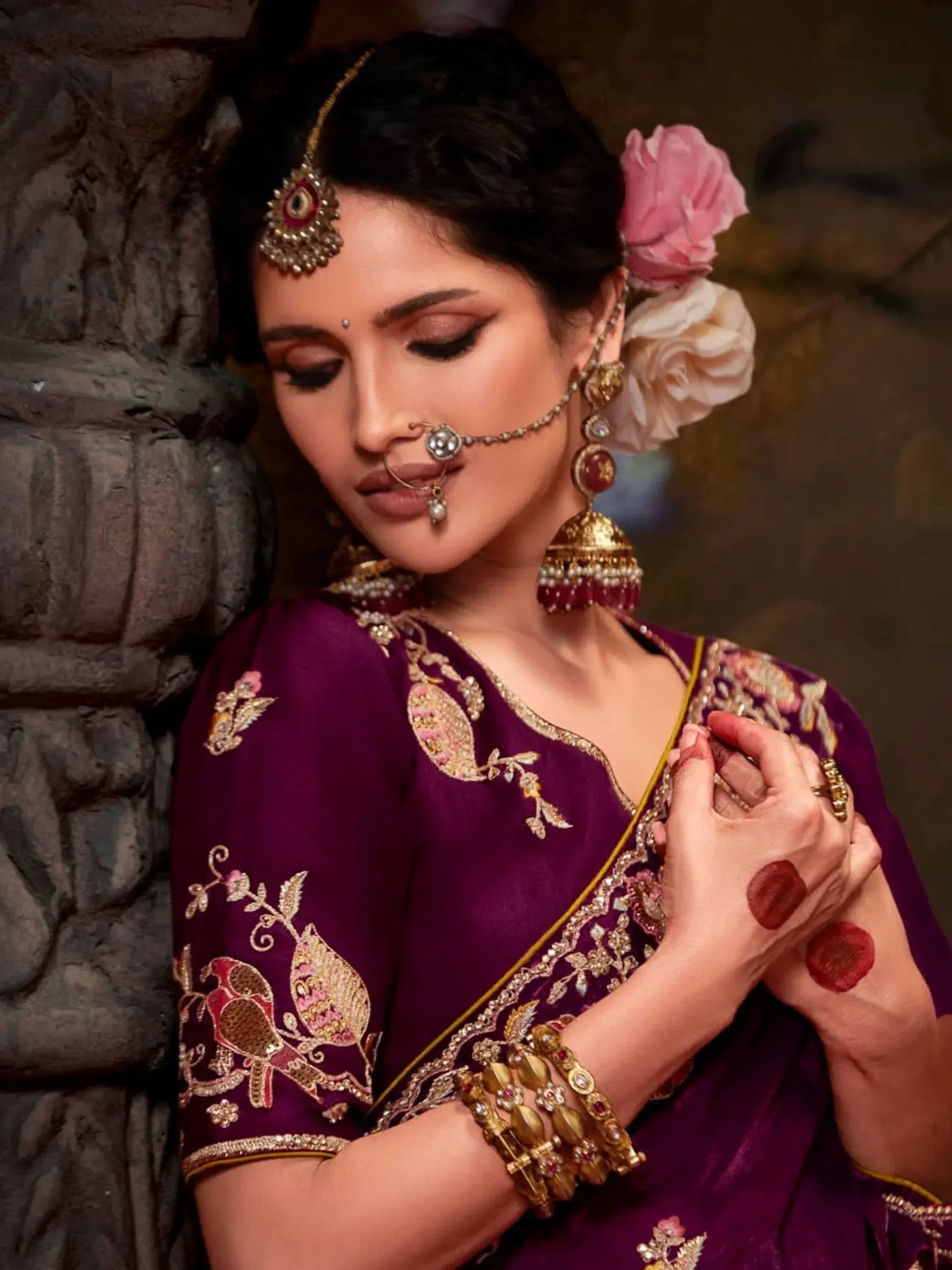 Elegant woman in purple embroidered saree with gold jewelry and floral hair accessory
