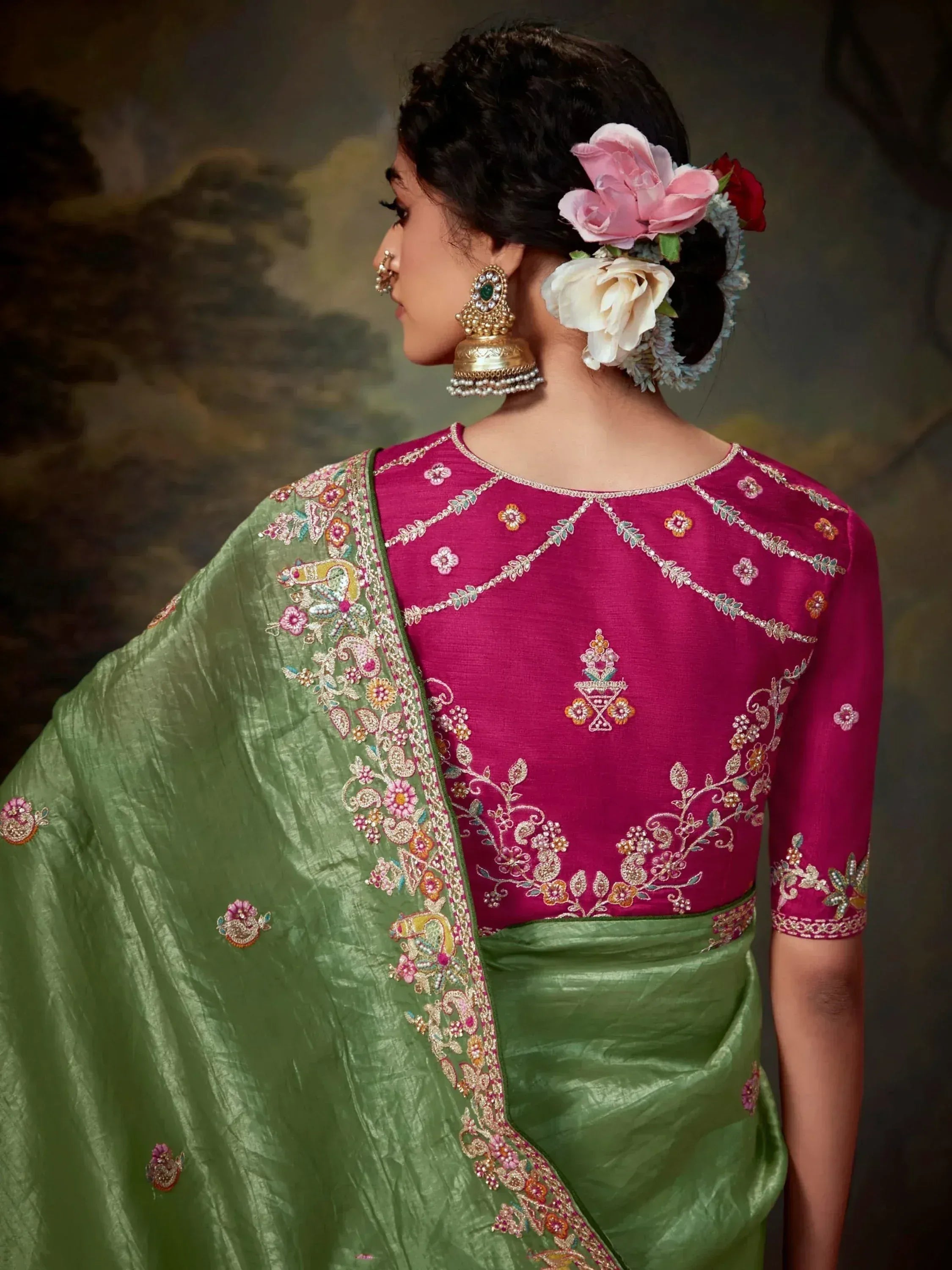 Woman in pink embroidered blouse with green saree, floral hair accessories, and traditional Indian jewelry
