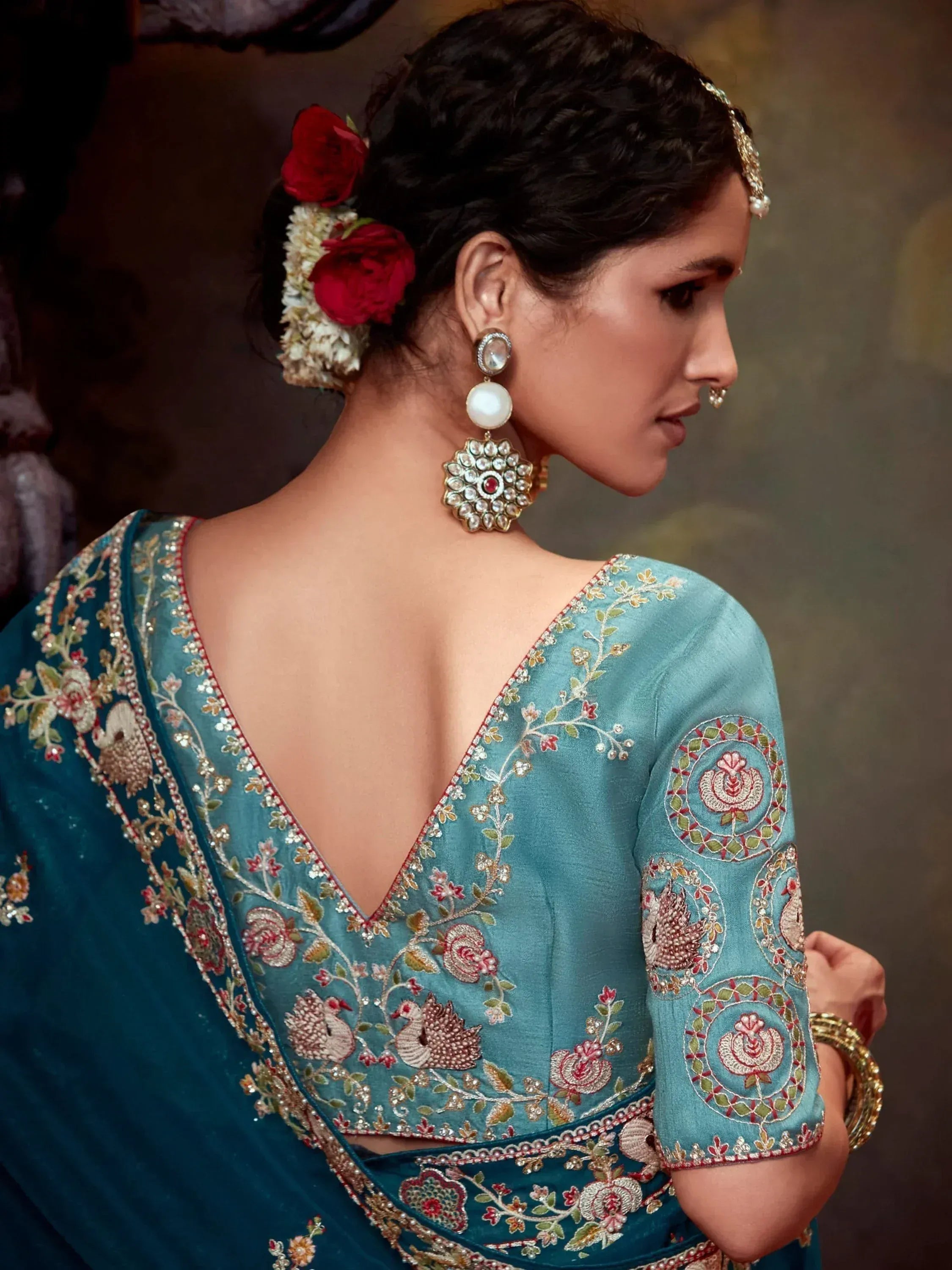 Teal embroidered saree with floral peacock motifs, backless blouse, and traditional jewelry for Indian ethnic wear