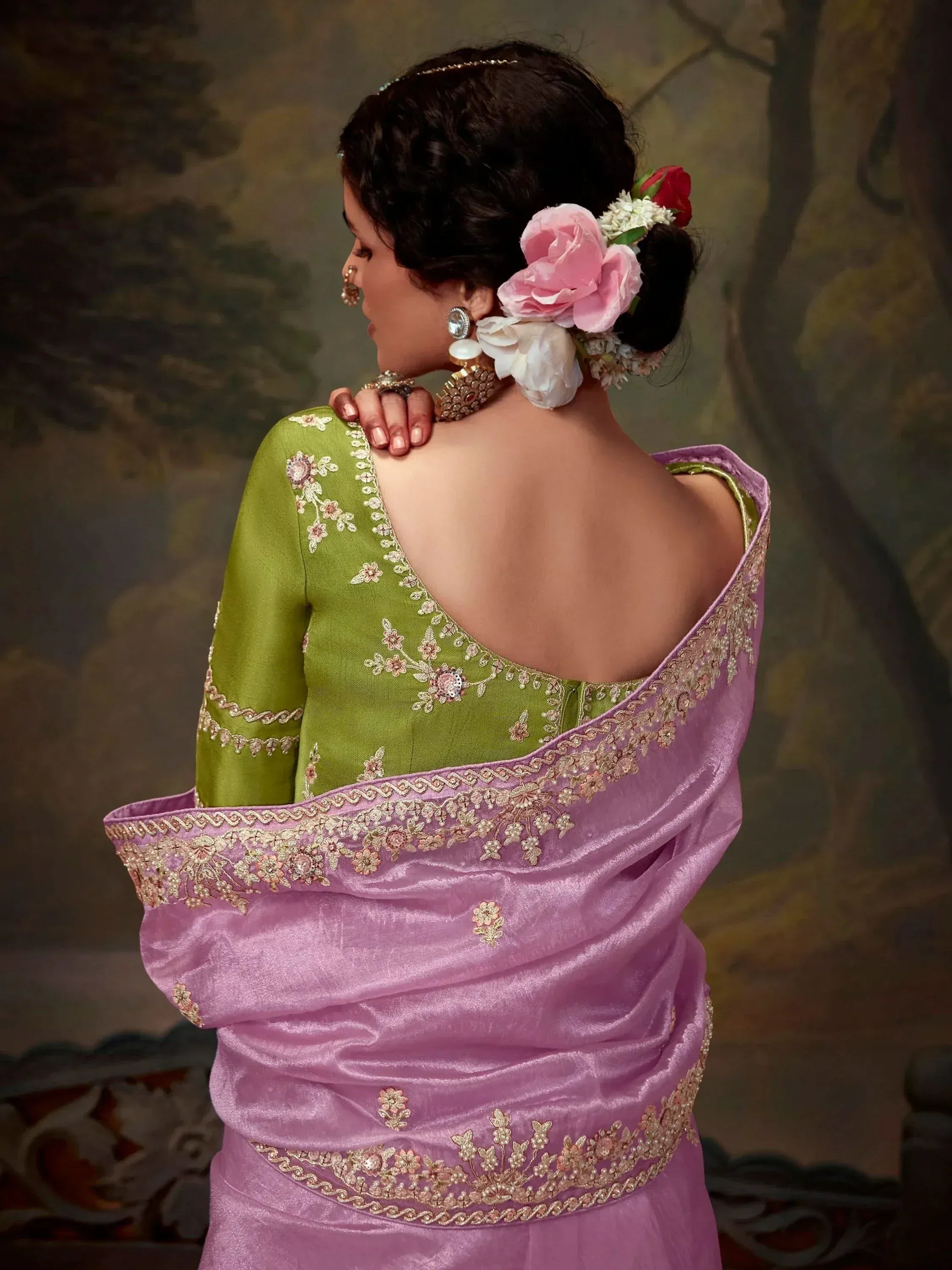 Woman in green embroidered blouse with pink saree, floral hair accessories, and traditional jewelry