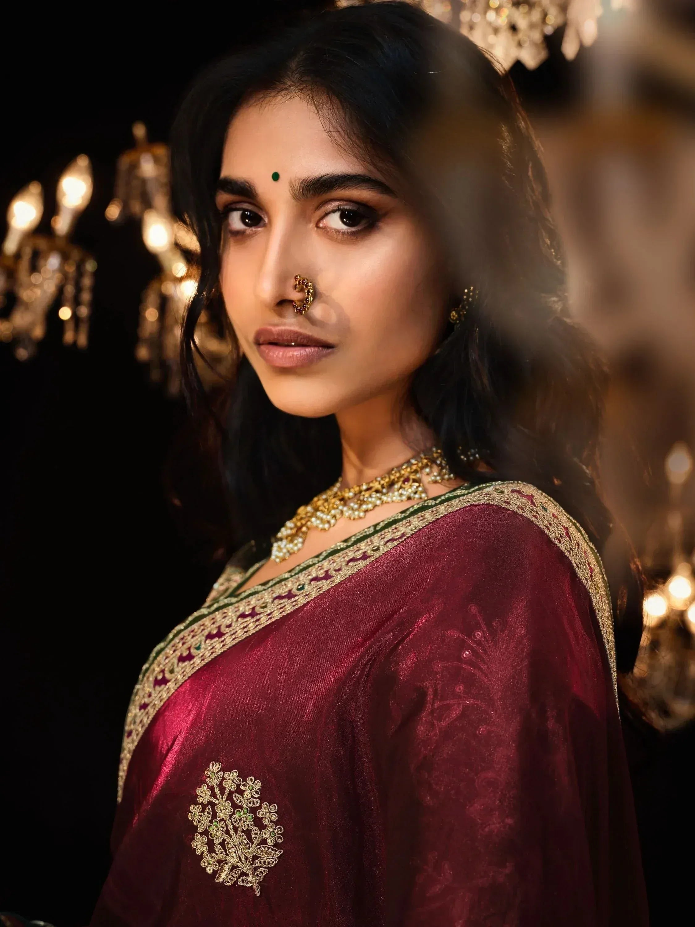 Woman in maroon ethnic saree with gold embroidery, traditional jewelry, and nose ring, perfect for Indian weddings or festivals.