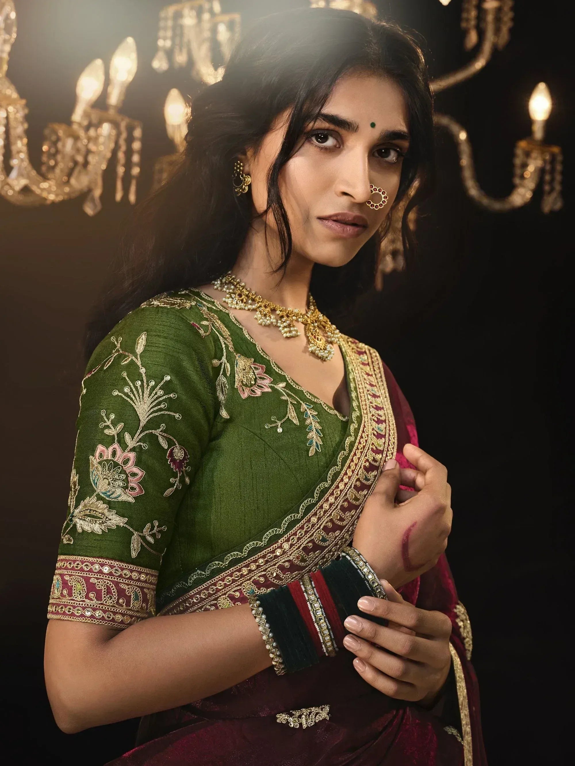 Woman in green and maroon embroidered saree with gold jewelry, perfect for Indian ethnic occasions.