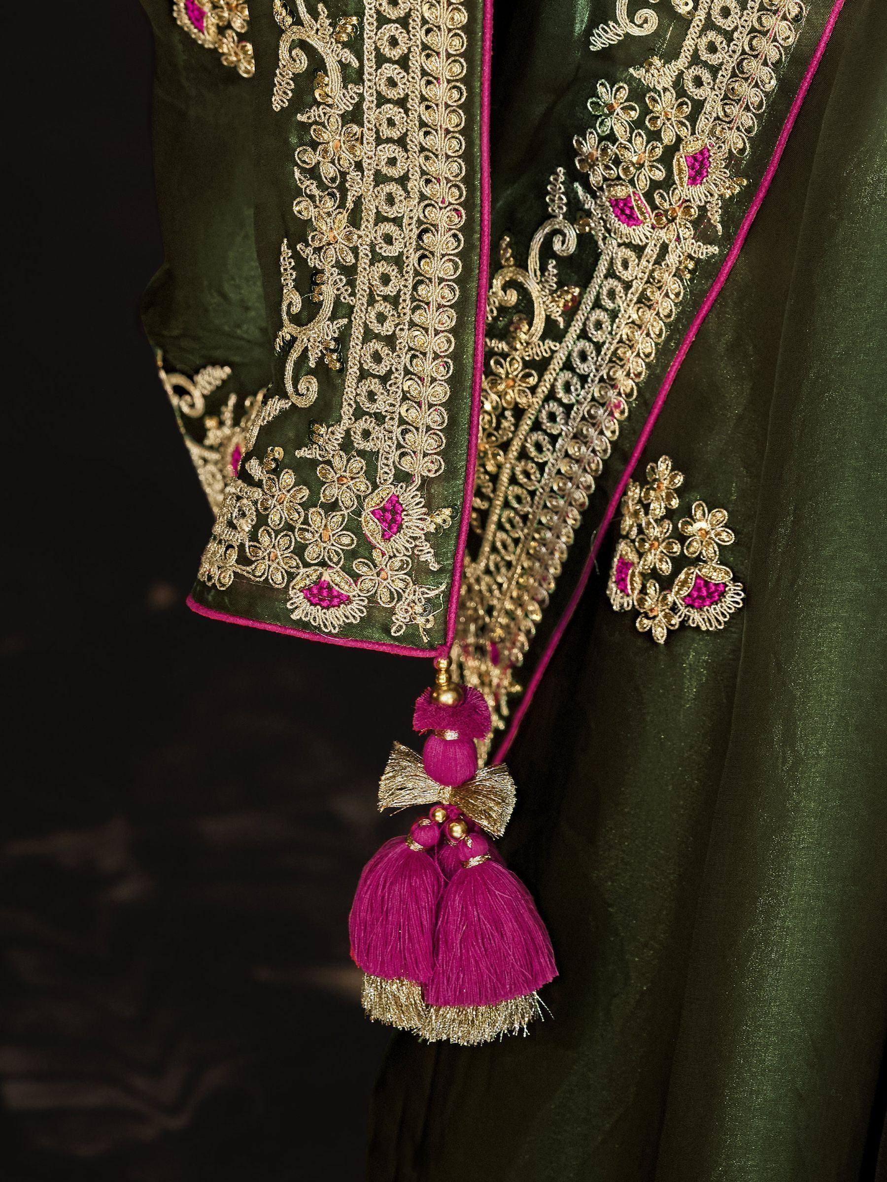 Green ethnic wear with gold embroidery, pink tassels, and floral detailing for festive occasions