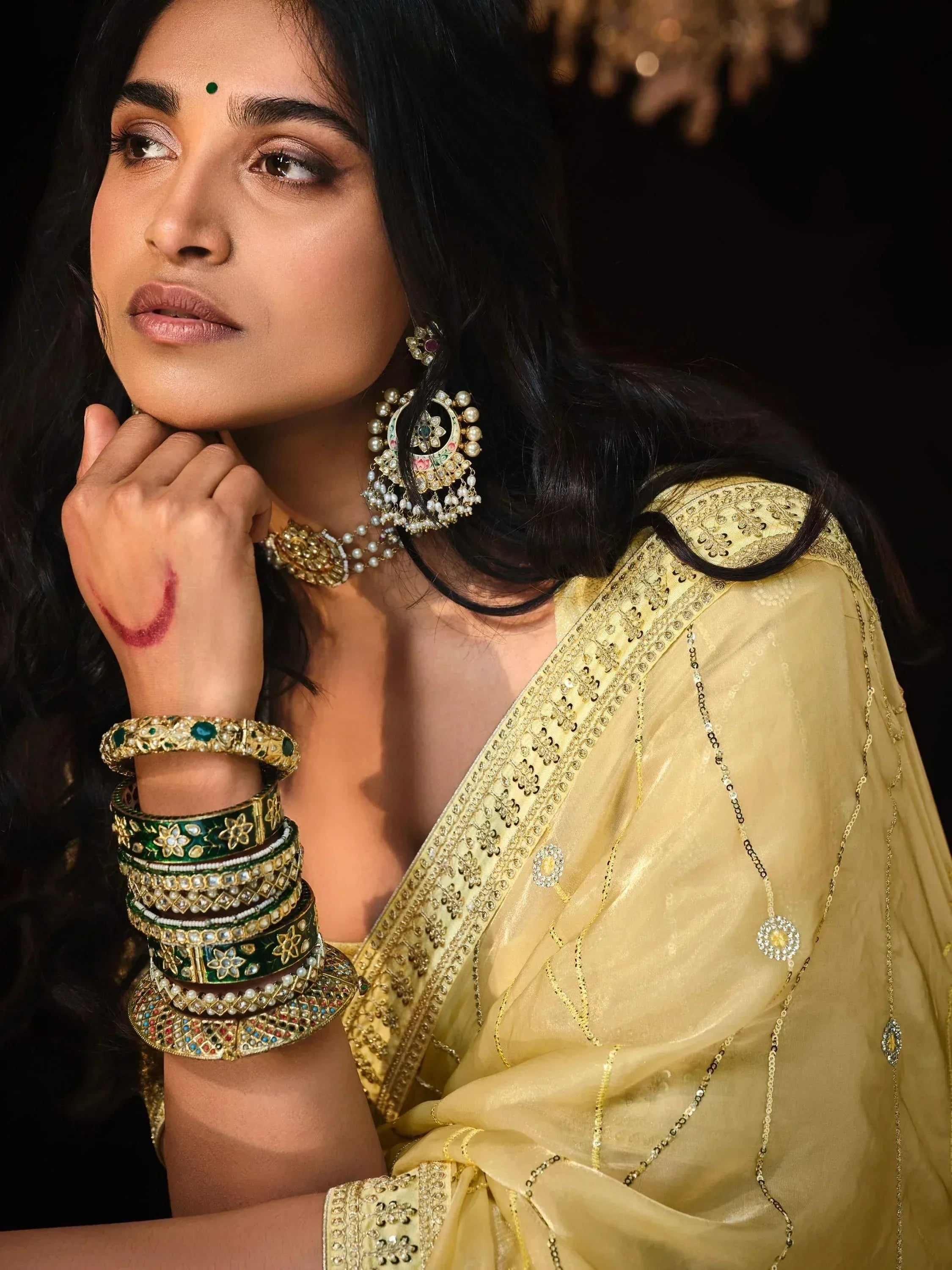 Elegant woman in golden ethnic wear with intricate embroidery, traditional jewelry, and bindi, showcasing Indian designer fashion.