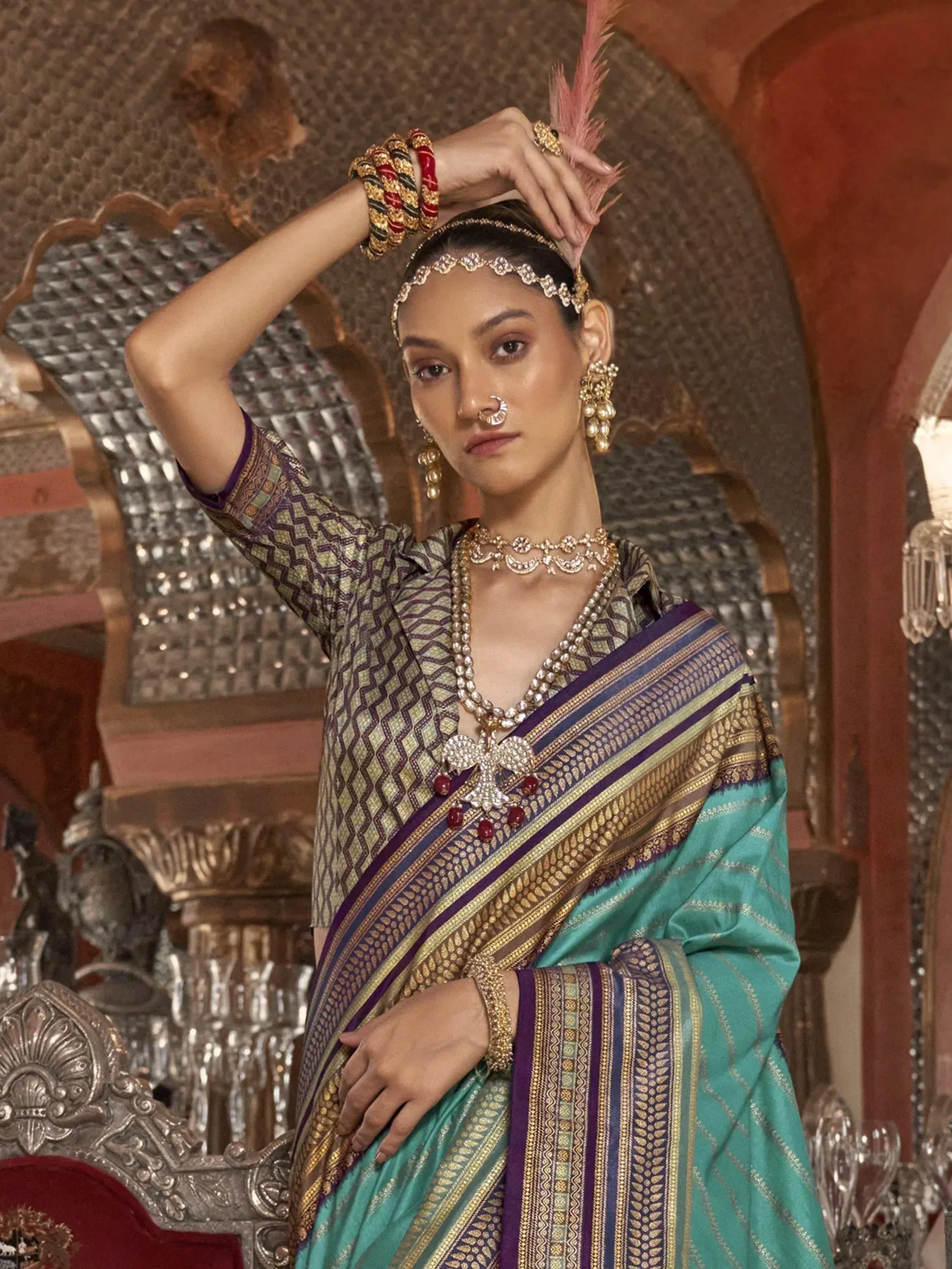 Elegant woman in traditional Indian saree with intricate gold embroidery, statement jewelry, and feather hair accessory