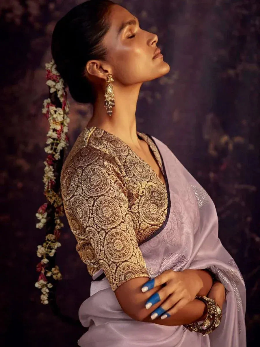 Woman in elegant lavender saree with gold embroidered blouse, floral hair accessory, and traditional jewelry