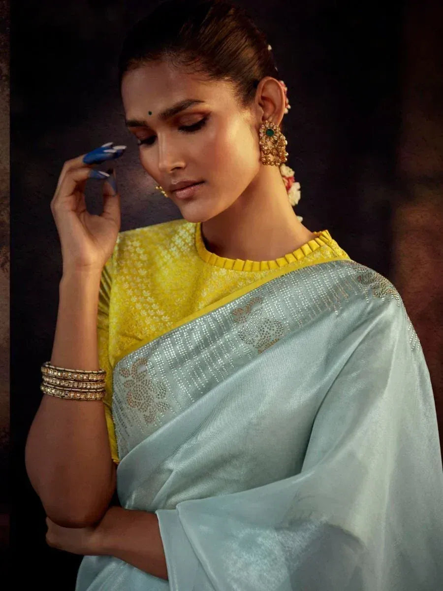 Elegant woman in light blue saree with yellow blouse, adorned with traditional jewelry, showcasing Indian ethnic wear.