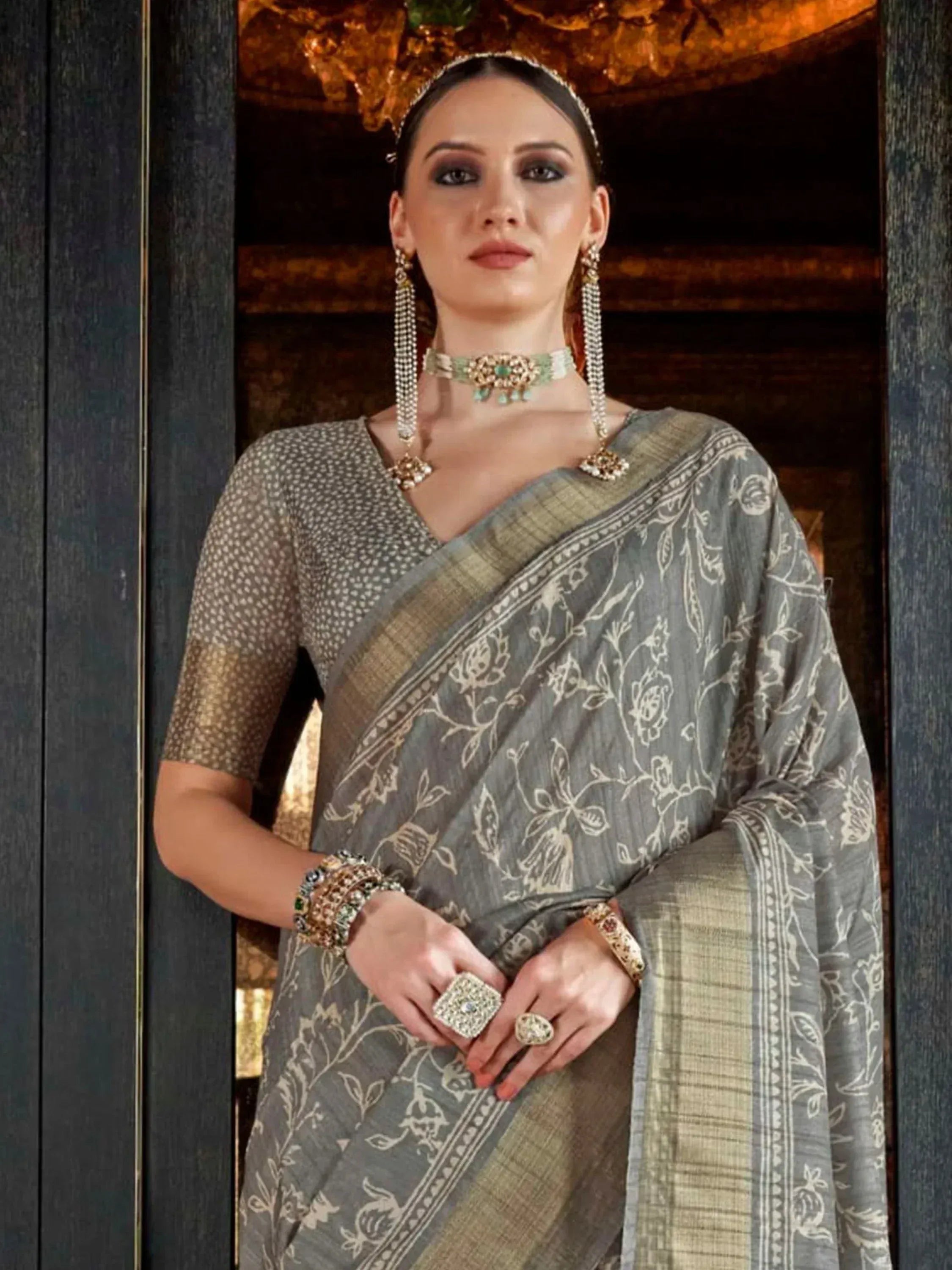 Grey floral print saree with gold border, paired with polka dot blouse and traditional jewelry for ethnic wear.